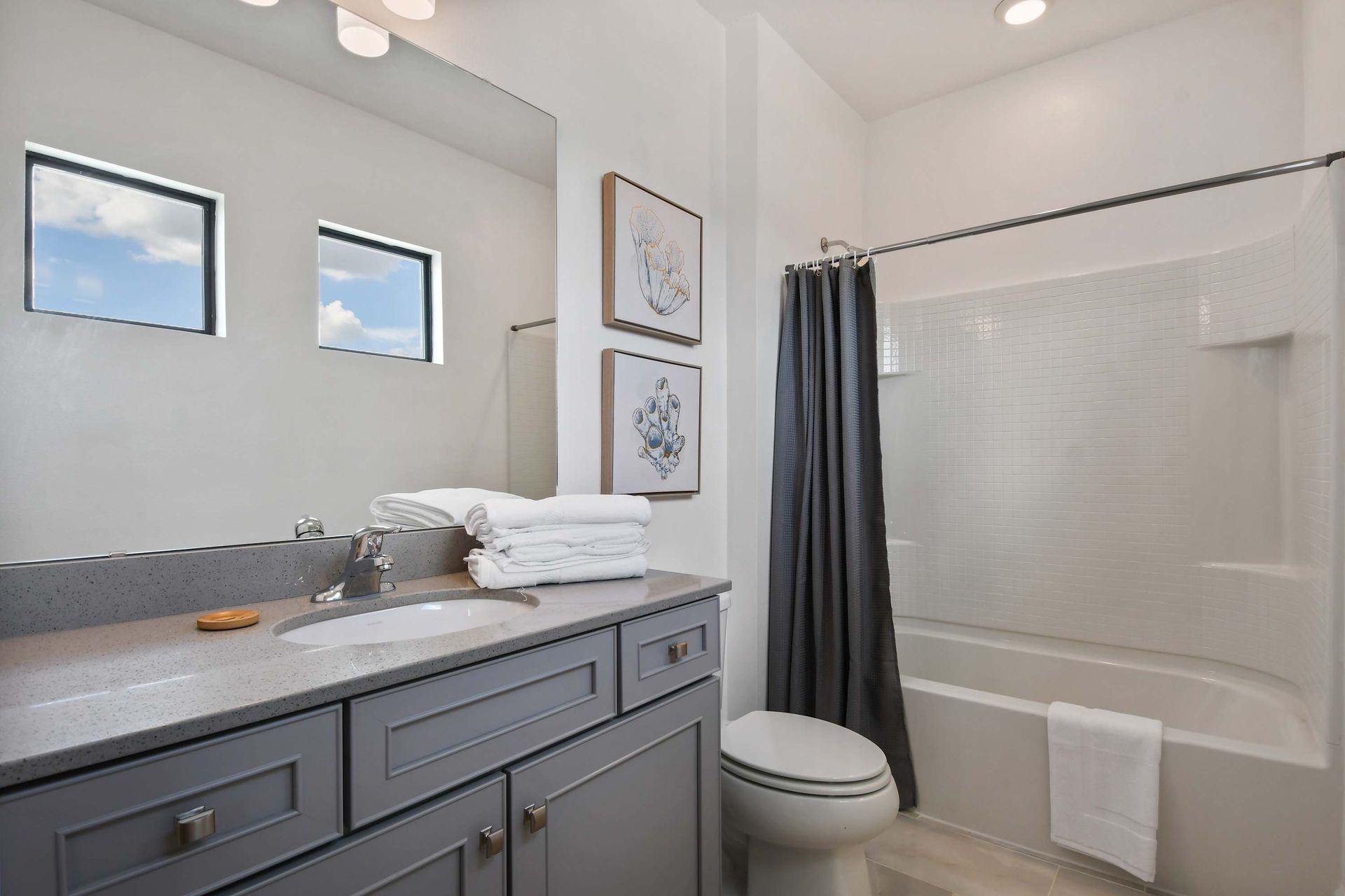 Bright full bathroom with double windows, coastal decor, and a sleek vanity design.