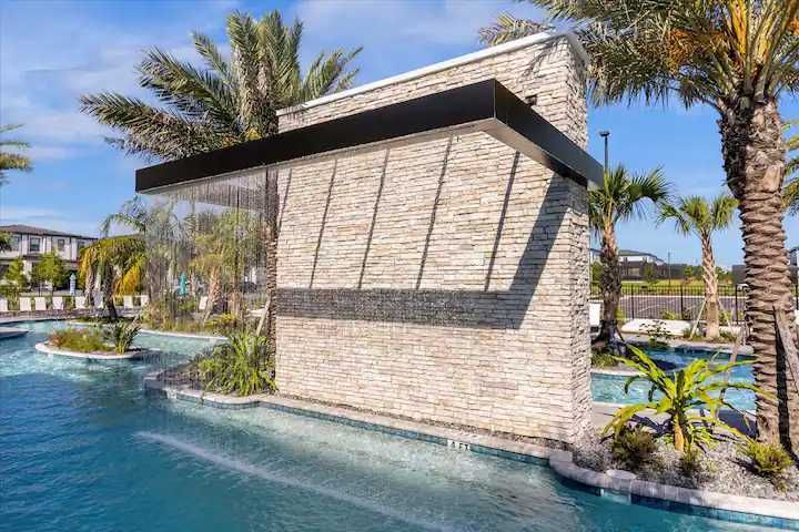 Relax beneath a modern waterfall feature in this palm-lined resort pool escape.
