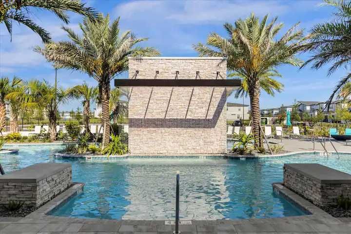 Serene pool with waterfall feature, surrounded by palms and luxury loungers.
