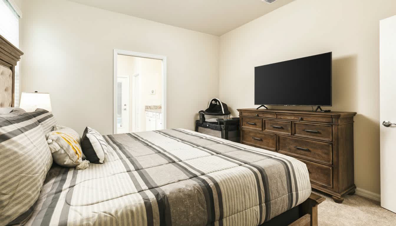 Elegant bedroom with neutral tones, featuring a large screen TV and cozy striped bedding.