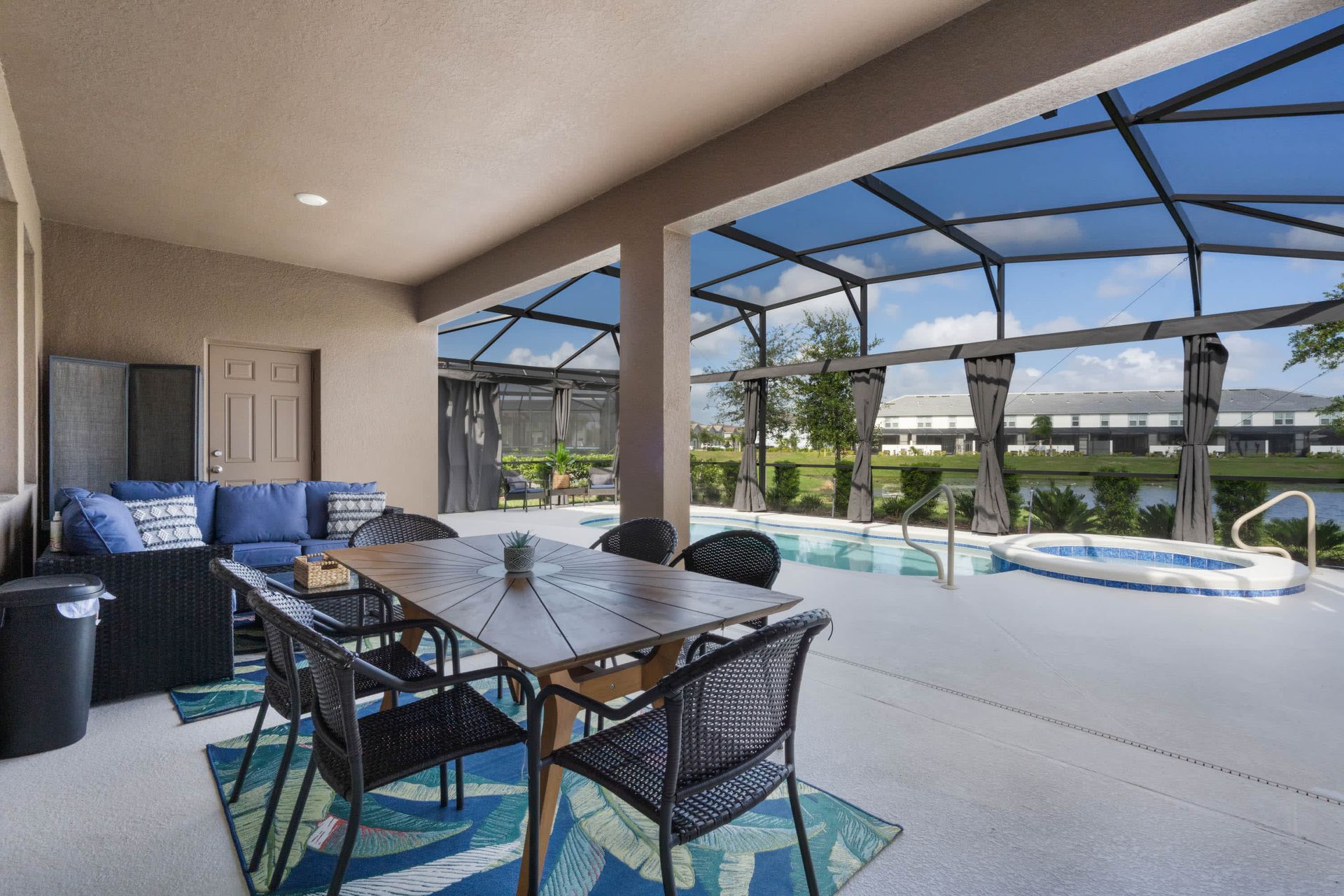 Covered lanai with dining table, comfy lounge seating, and screened pool with spa.