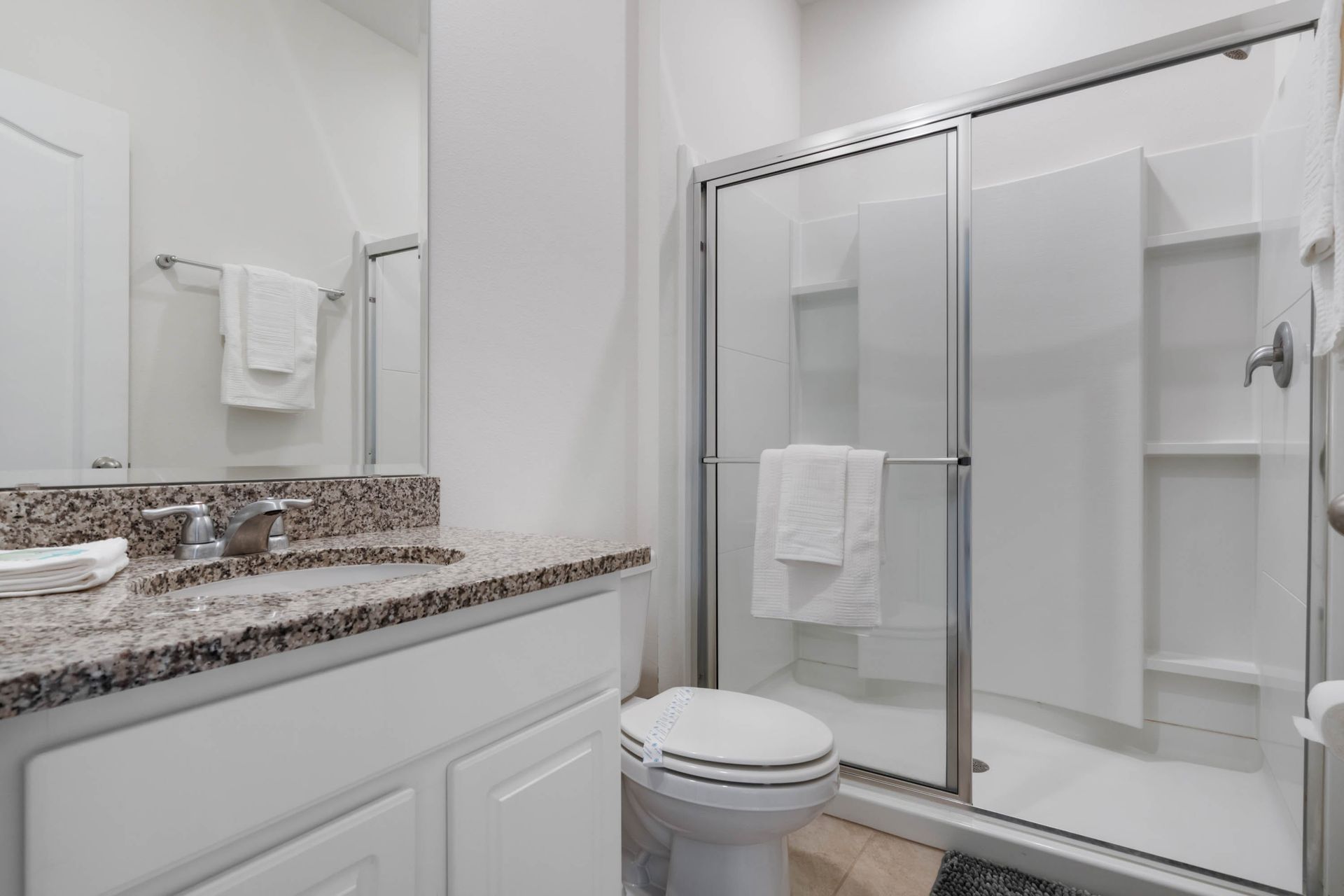 Crisp modern bathroom with granite vanity, glass walk-in shower, and fresh white towels.