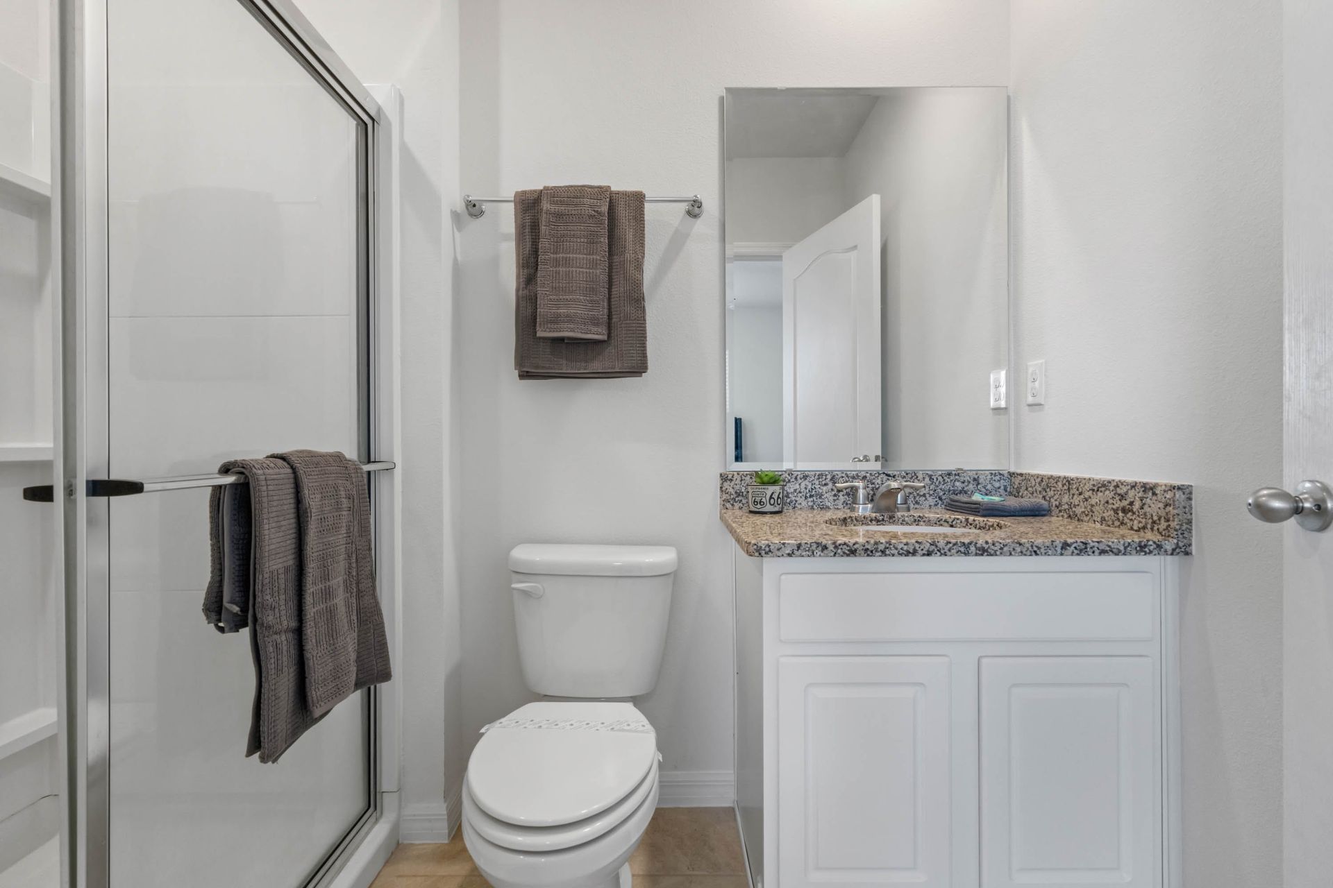 Modern bathroom with granite vanity, glass walk-in shower, and fresh neutral tones.