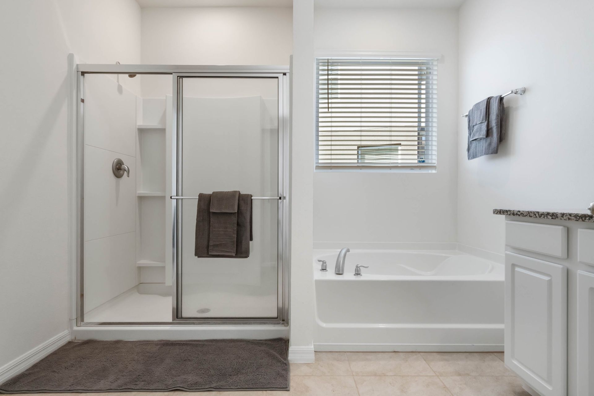 Spacious bathroom with glass walk-in shower, soaking tub, granite vanity, and soft lighting.