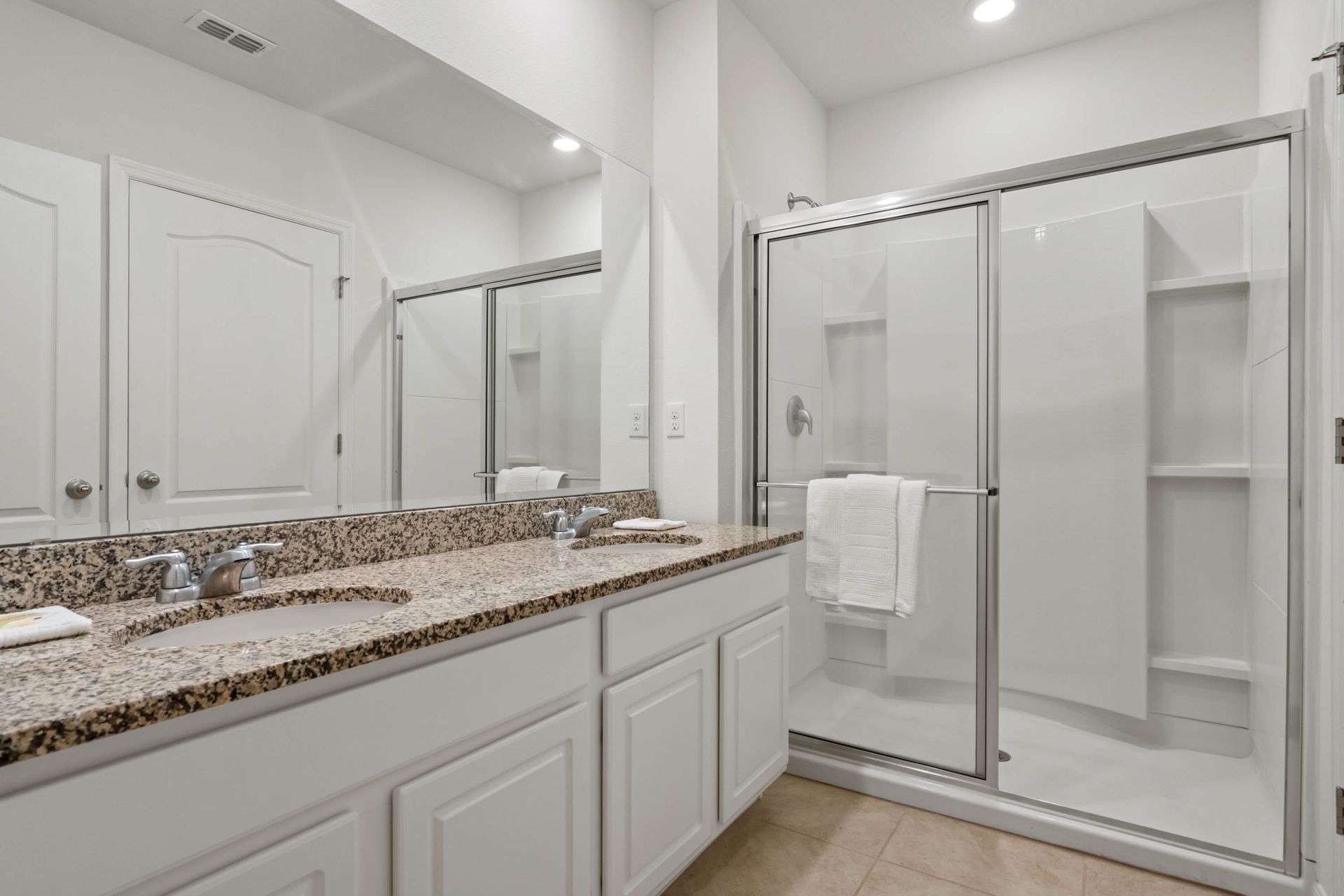 Bright modern bathroom with granite double vanity, glass walk-in shower, and sleek design.