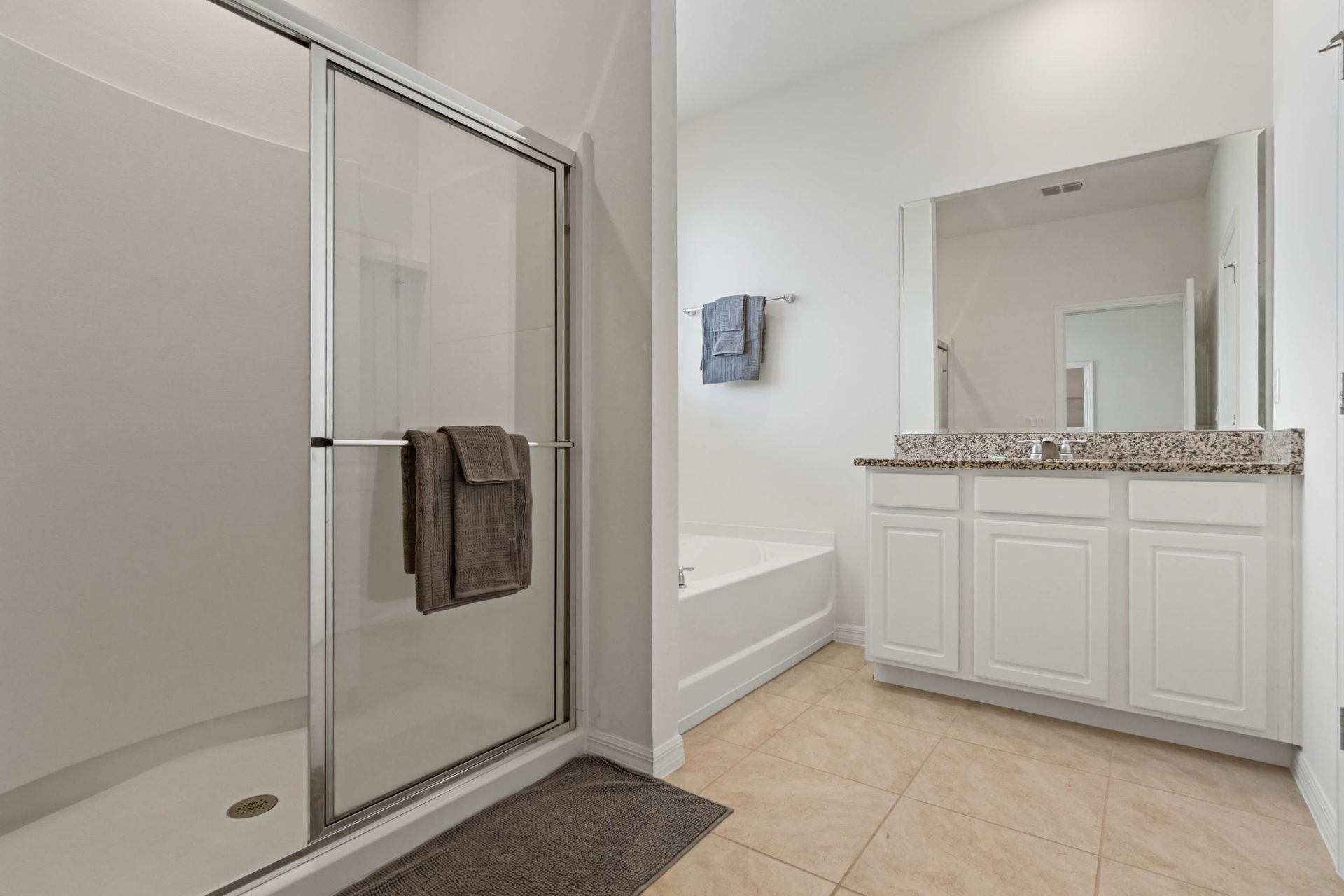 Spacious bathroom with granite vanity, glass shower, soaking tub, and neutral tones.