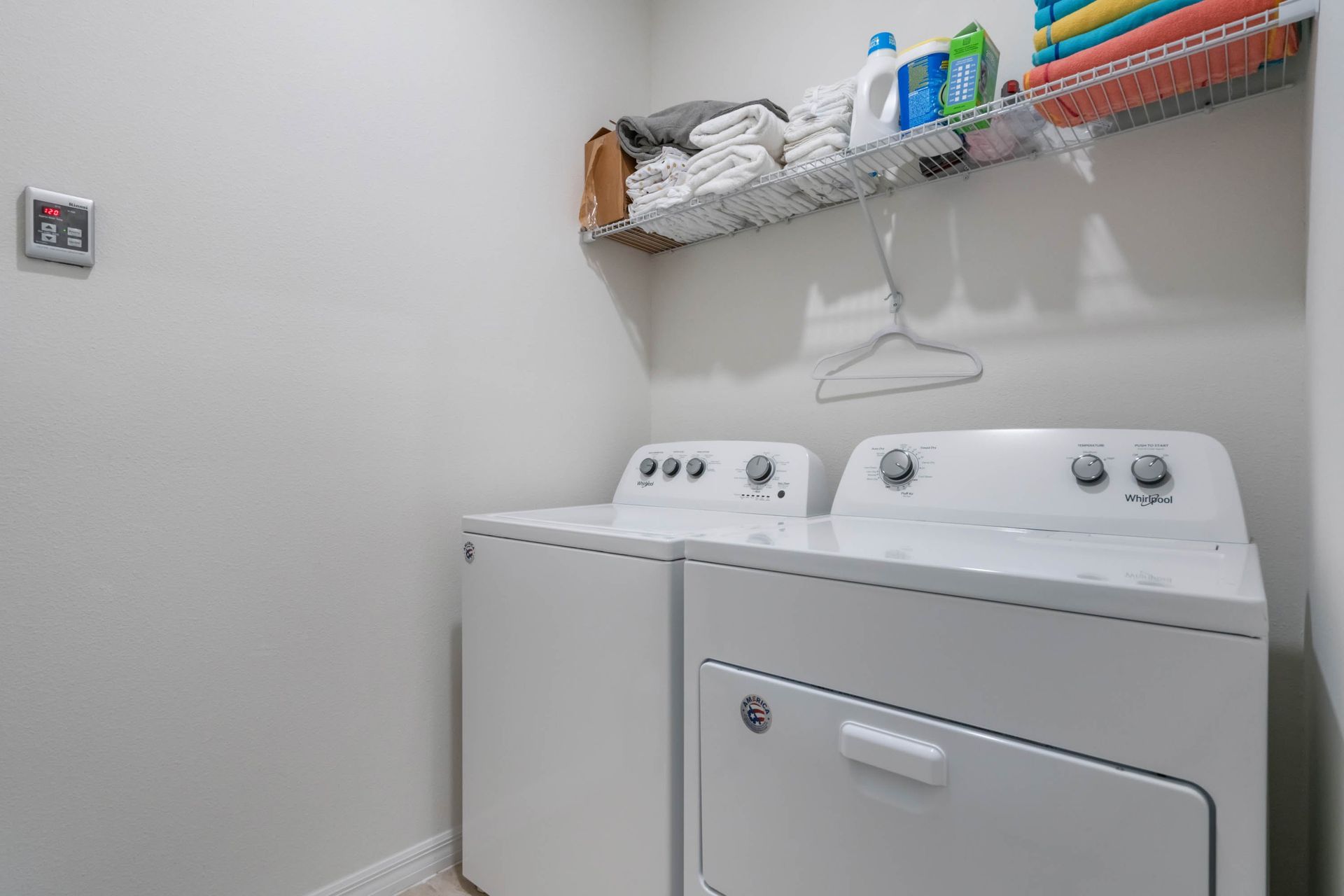 Dedicated laundry room with washer, dryer, and overhead storage stocked with essentials.