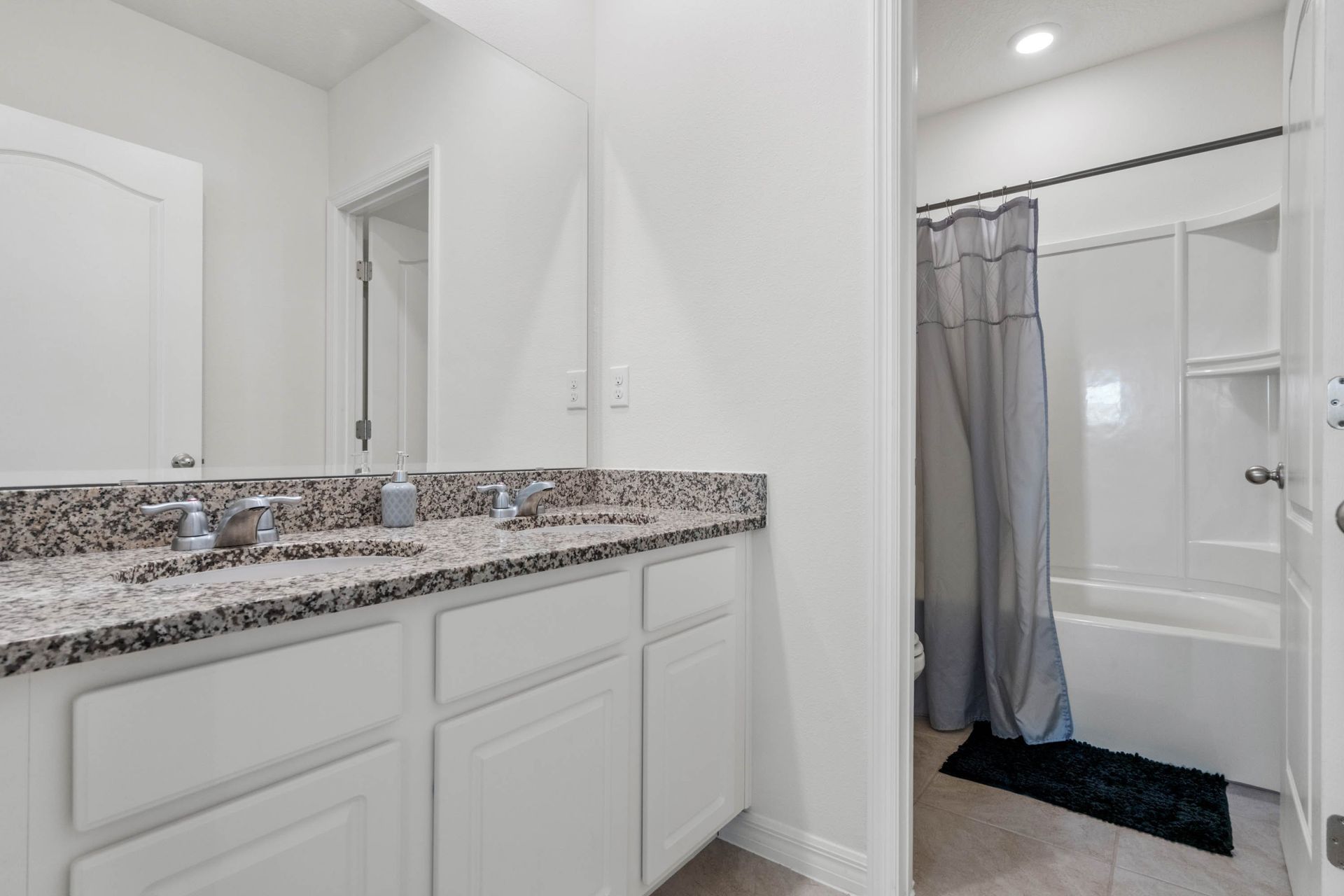 Modern bathroom with granite double vanity, full tub-shower combo, and bright lighting.