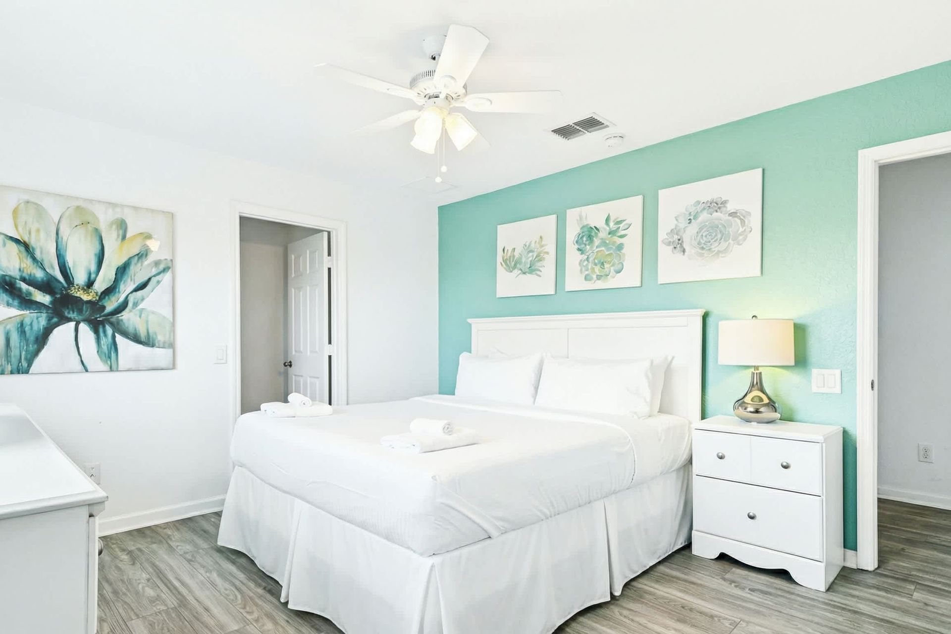 Fresh and airy queen bedroom with soft tones, floral art, and a flat-screen TV.