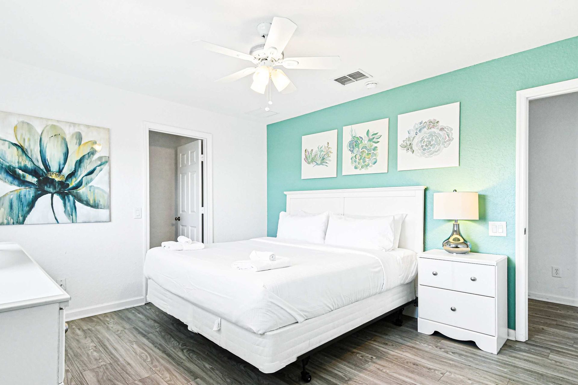 Fresh and airy queen bedroom with soft tones, floral art, and a flat-screen TV.