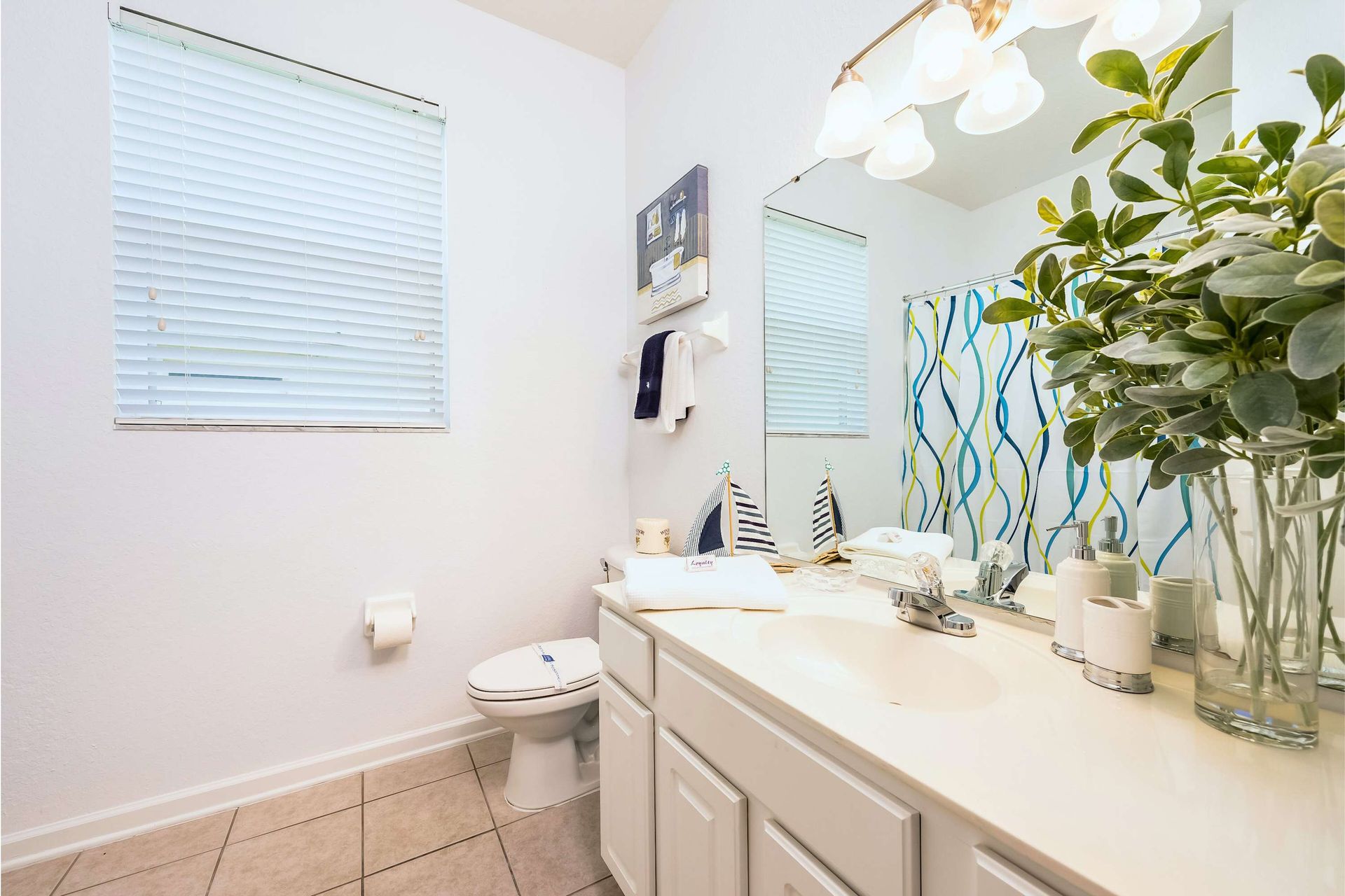 Bright and cheerful bathroom featuring a large mirror, modern lighting, nautical-themed accents, and a colorful wavy-patterned shower curtain.