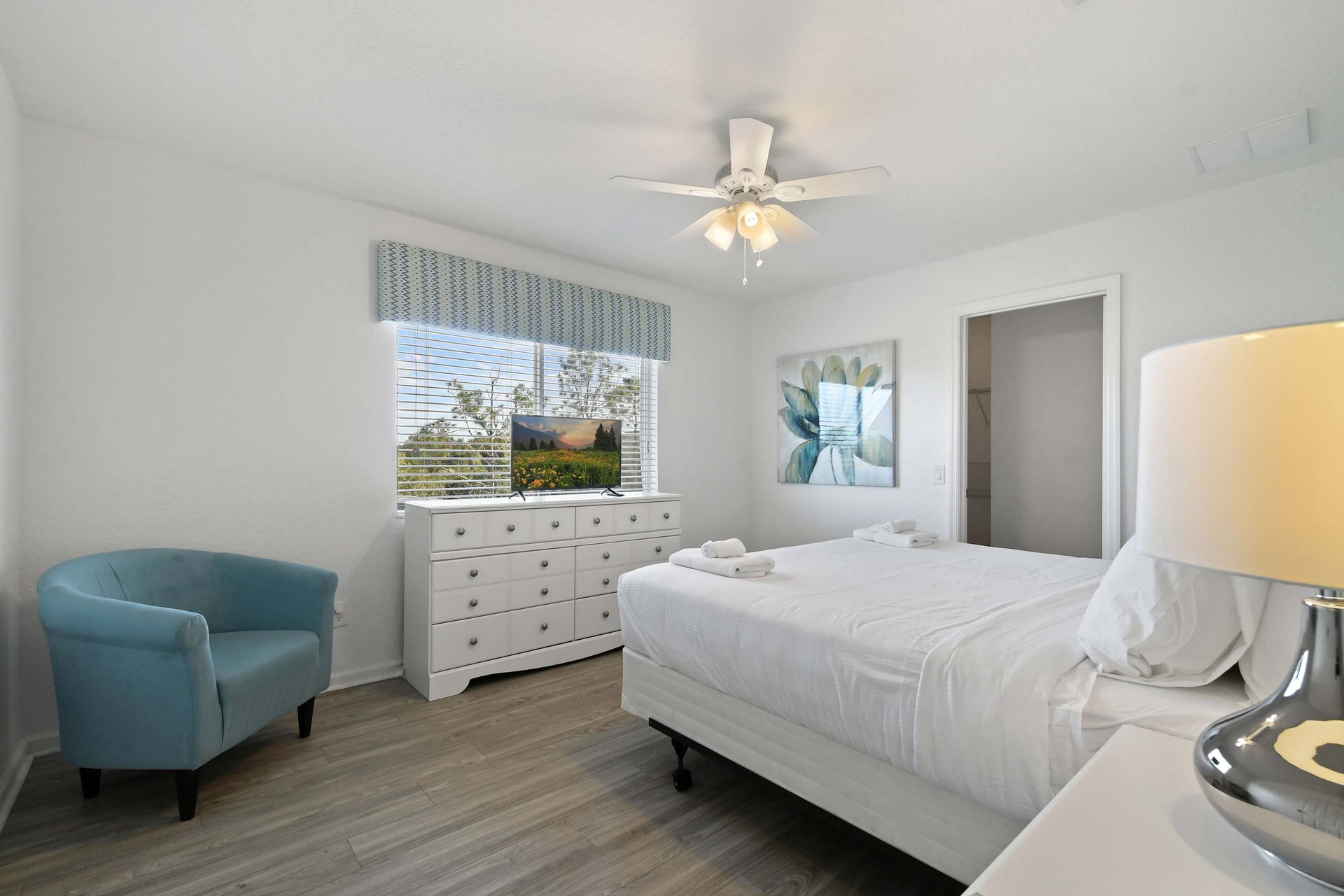 Bright queen bedroom with coastal charm, flat-screen TV, and walk-in closet access.