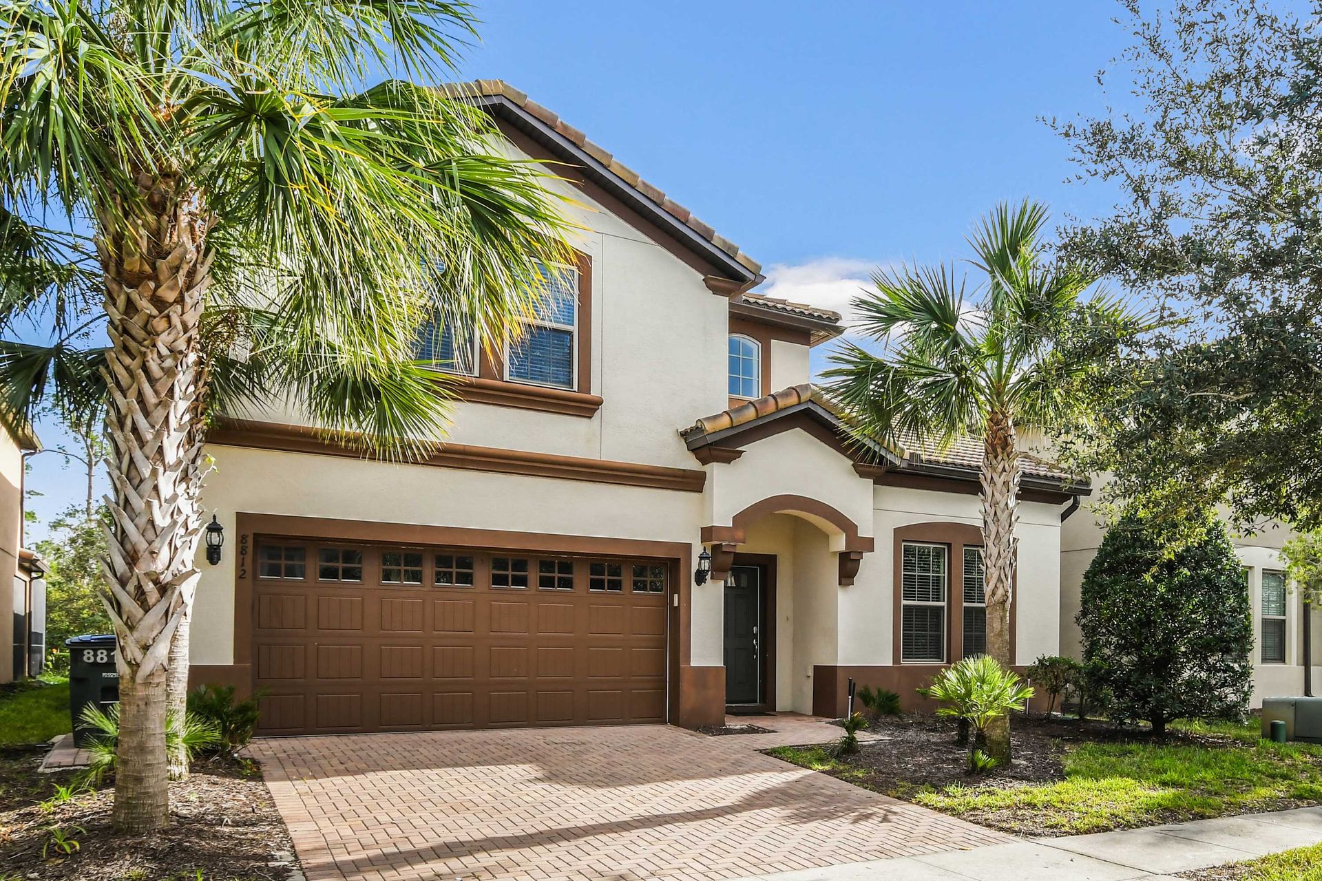 Charming two-story home with palm trees, paved driveway, and Mediterranean style.