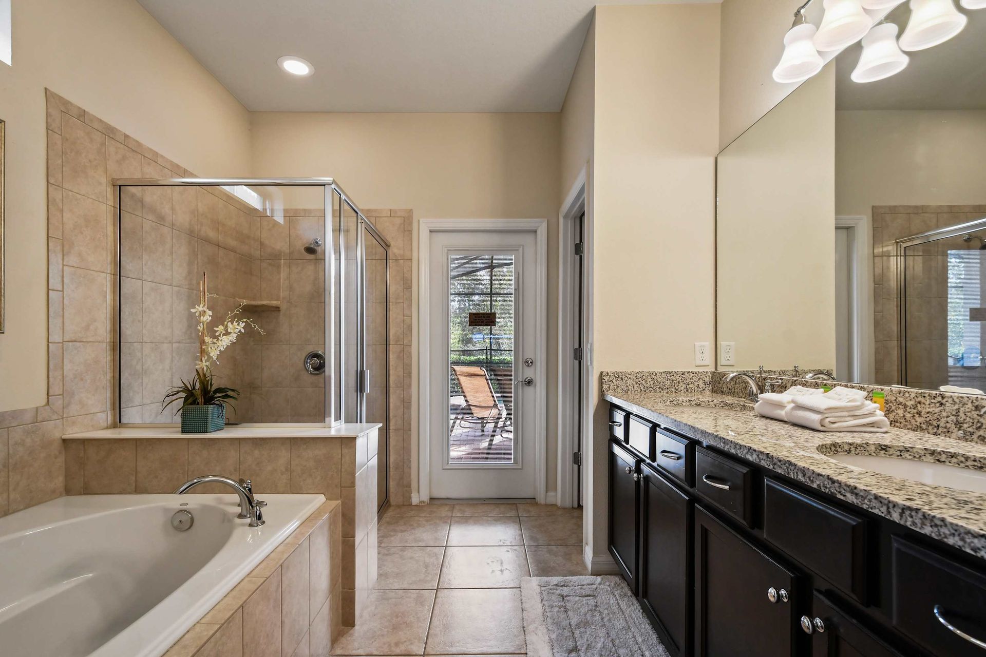 Spacious bathroom with dual sinks, walk-in shower, tub, and poolside access.