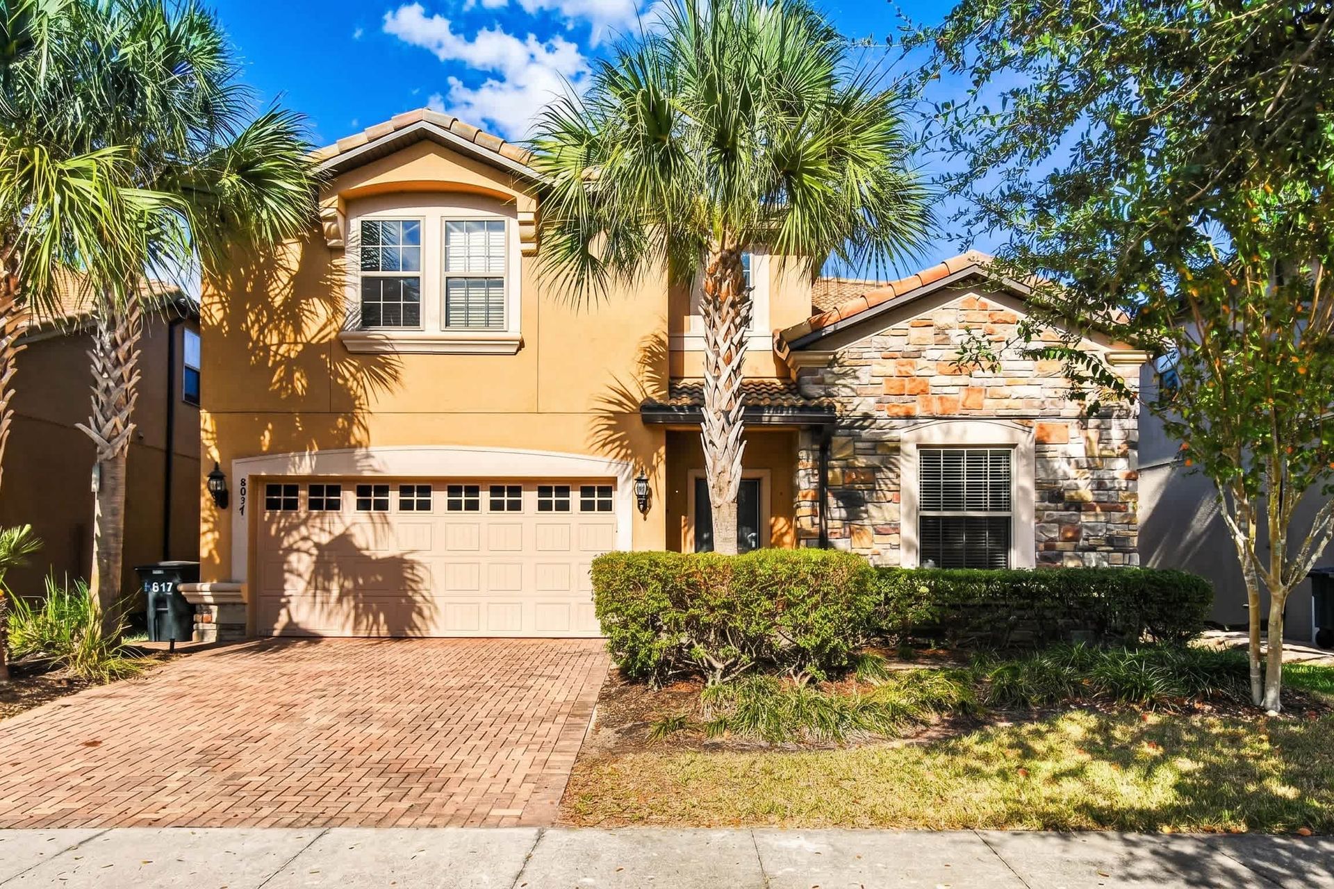 Beautiful villa with palm trees, stone accents, and spacious driveway in sunny setting.