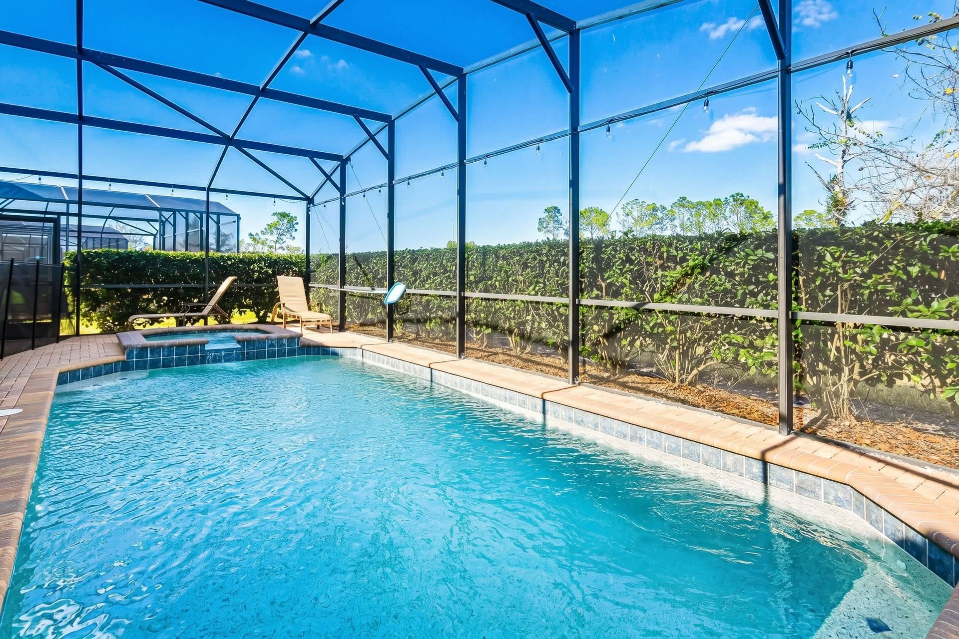Private screened pool with spa, sun loungers, and lush greenery for relaxing days.
