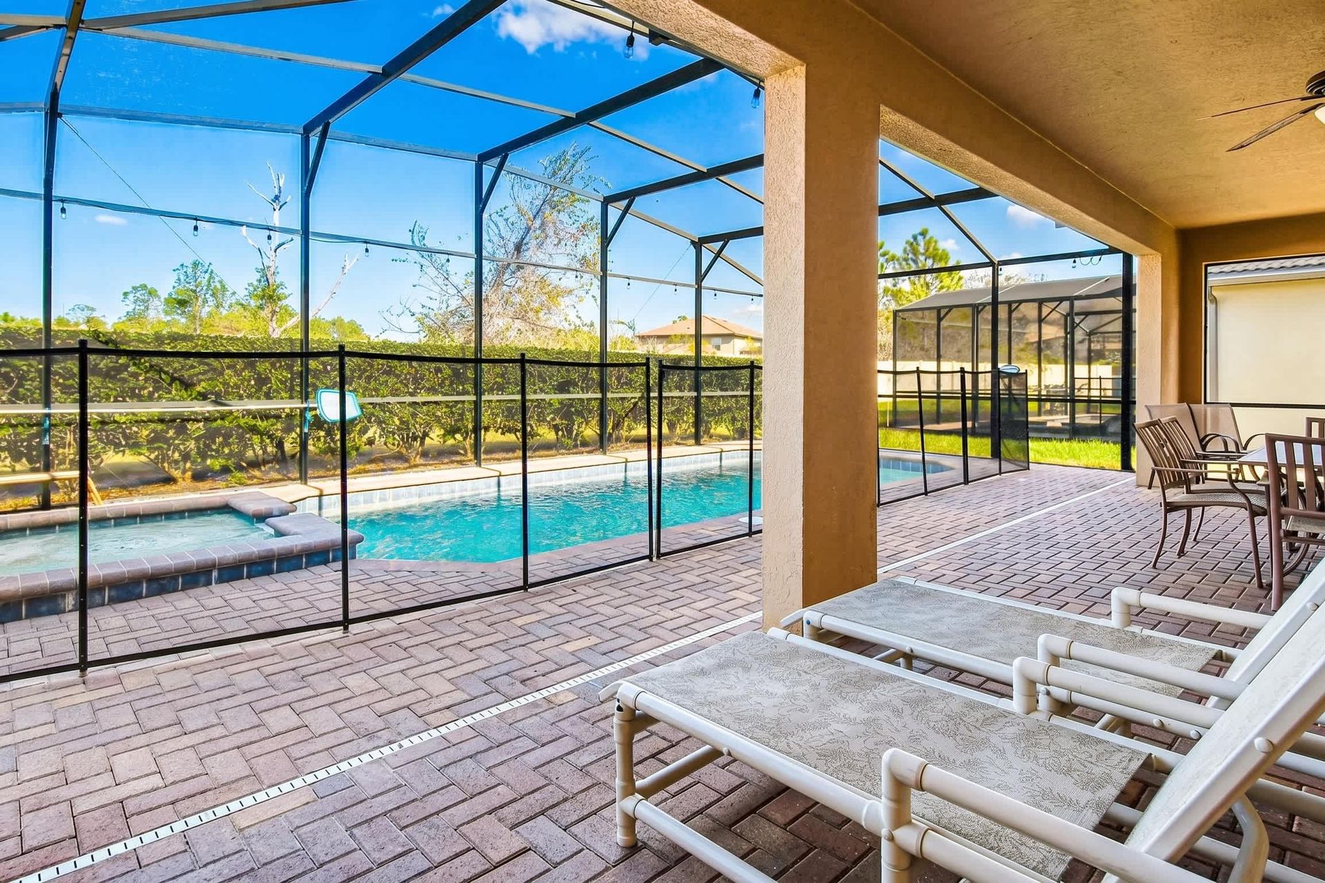 Covered patio with dining area, lounge chairs, ceiling fan, and screened pool view.