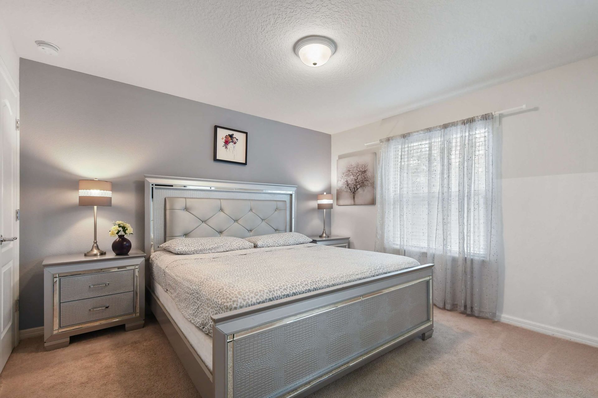 Elegant bedroom with king bed, stylish silver accents, and soft natural lighting.