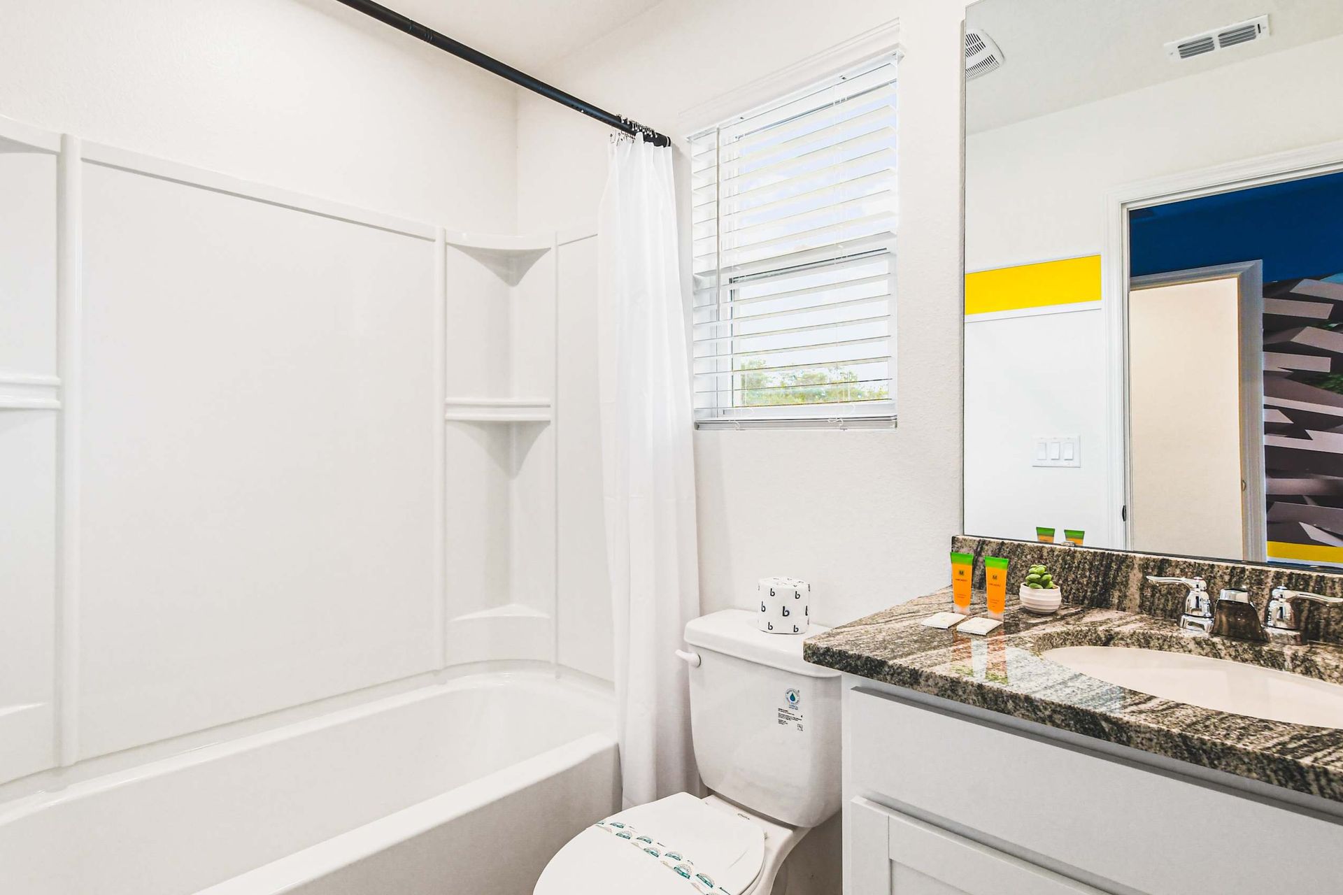 Bathroom with tub/shower combo and granite vanity near colorful themed room.