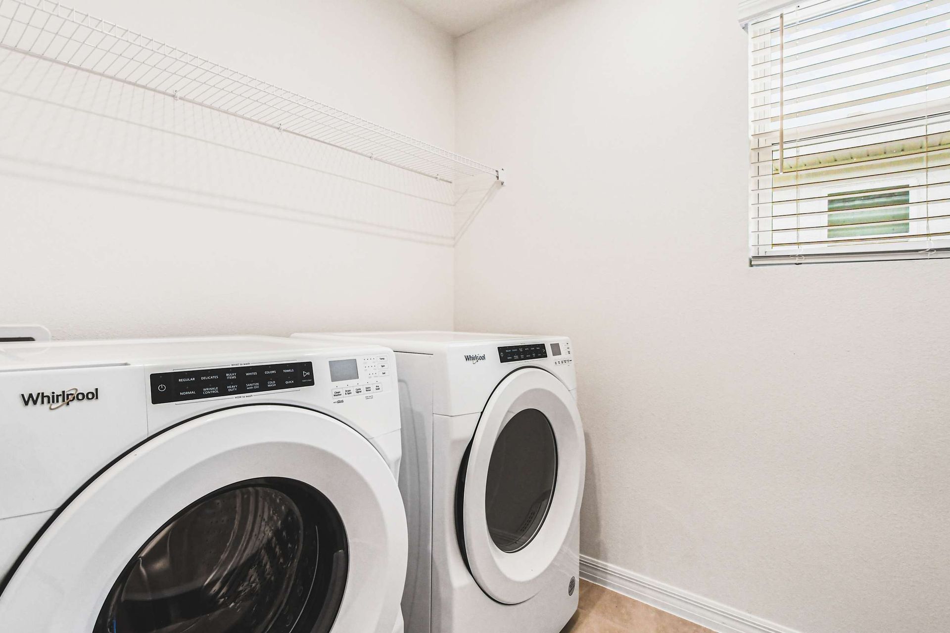Full laundry room with washer, dryer, shelving, and natural light from window.