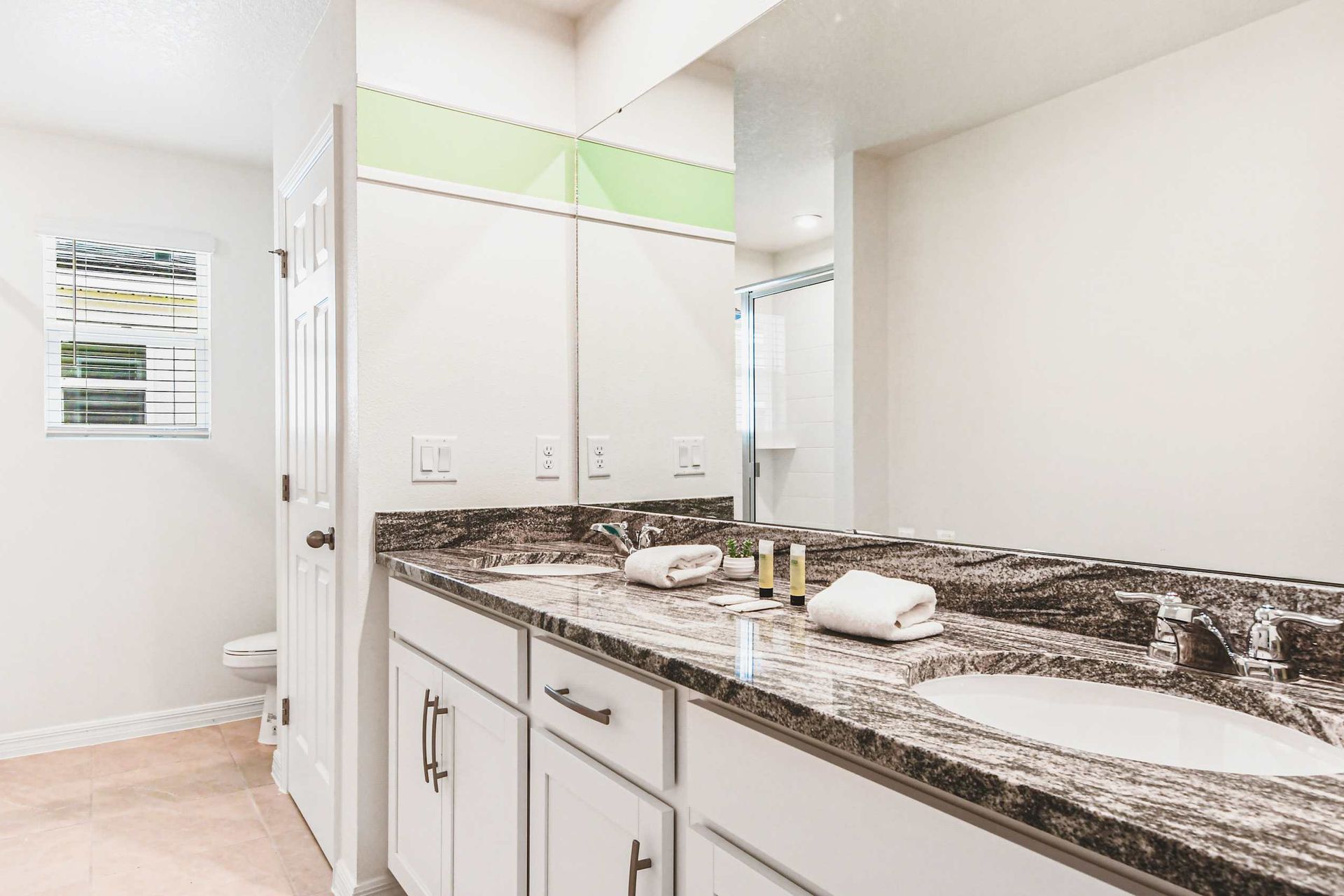 Elegant bathroom with dual granite sinks, glass shower, and natural light.