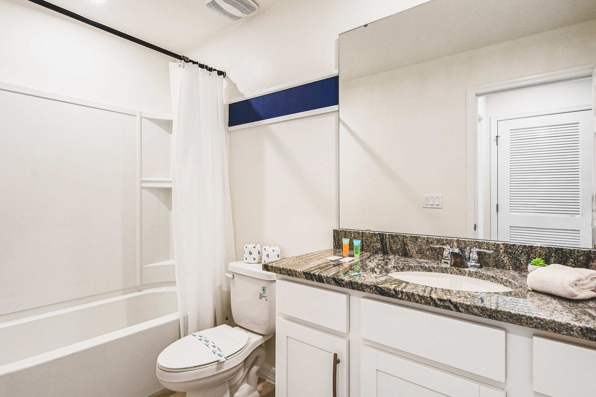 Bright bathroom with tub/shower combo, granite counter, and fresh towels provided.