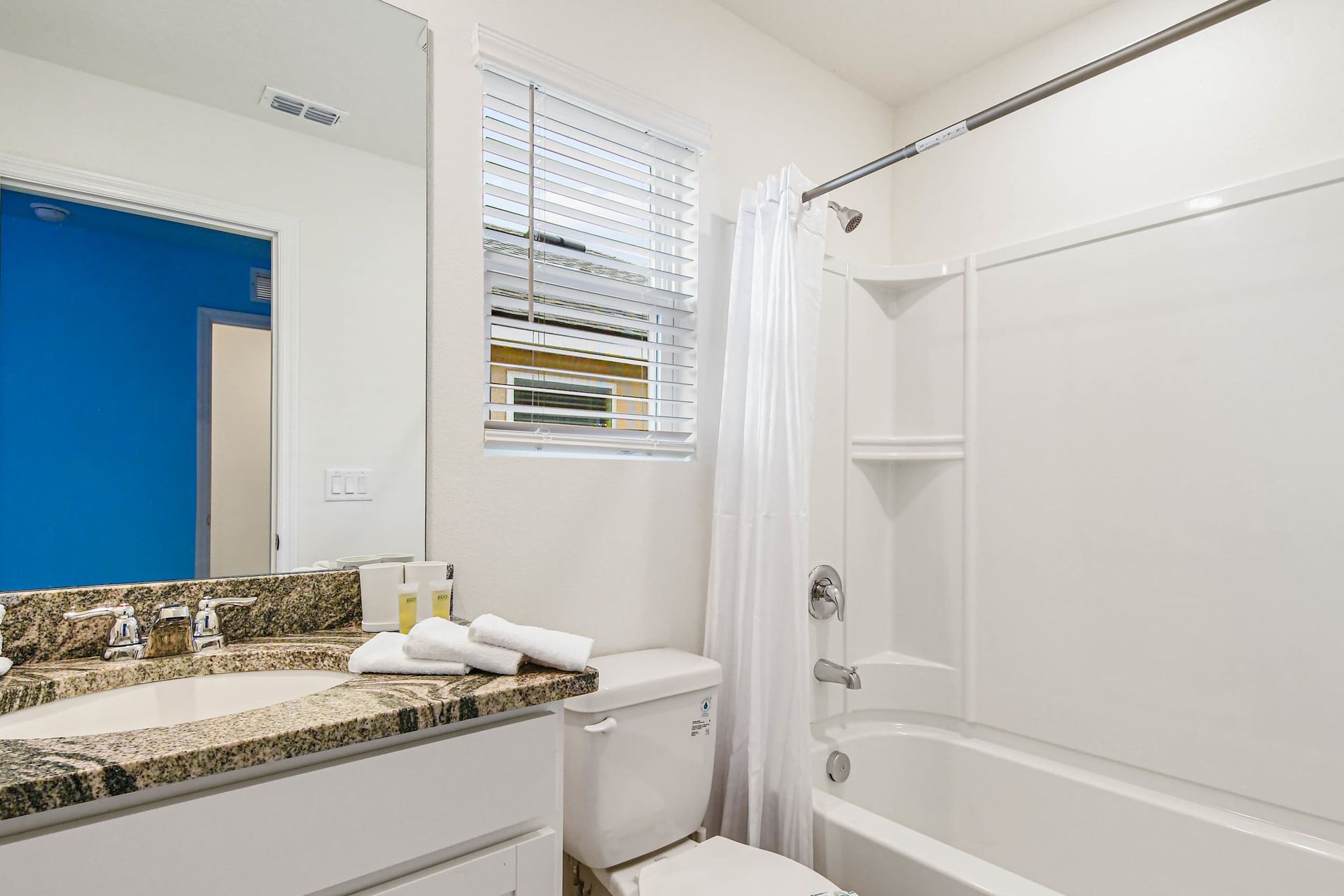 Fresh bright bathroom with granite countertop, large mirror, and a clean tub-shower combo.