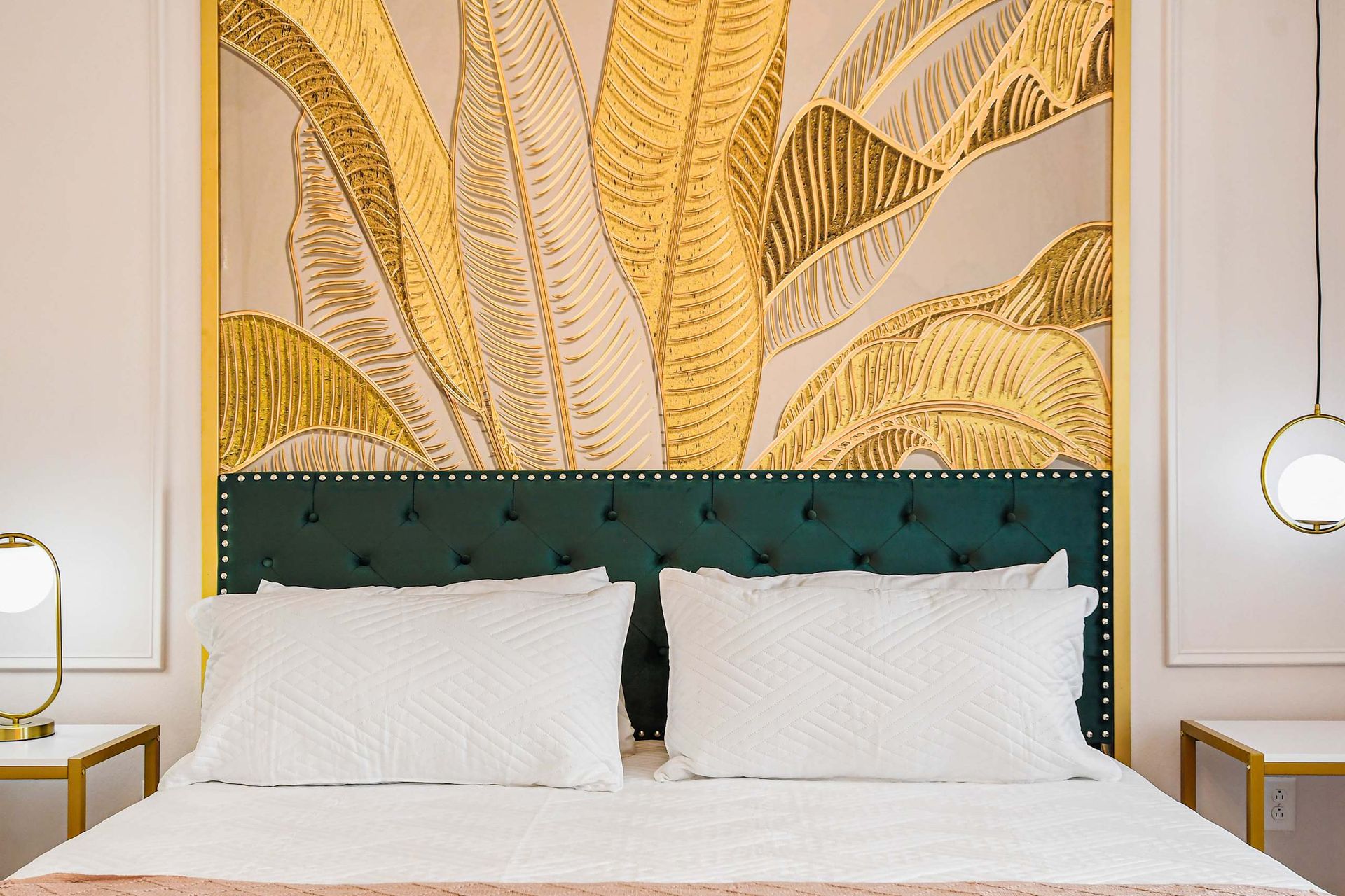 Luxurious bedroom with emerald headboard, gold leaf mural, and elegant lighting.