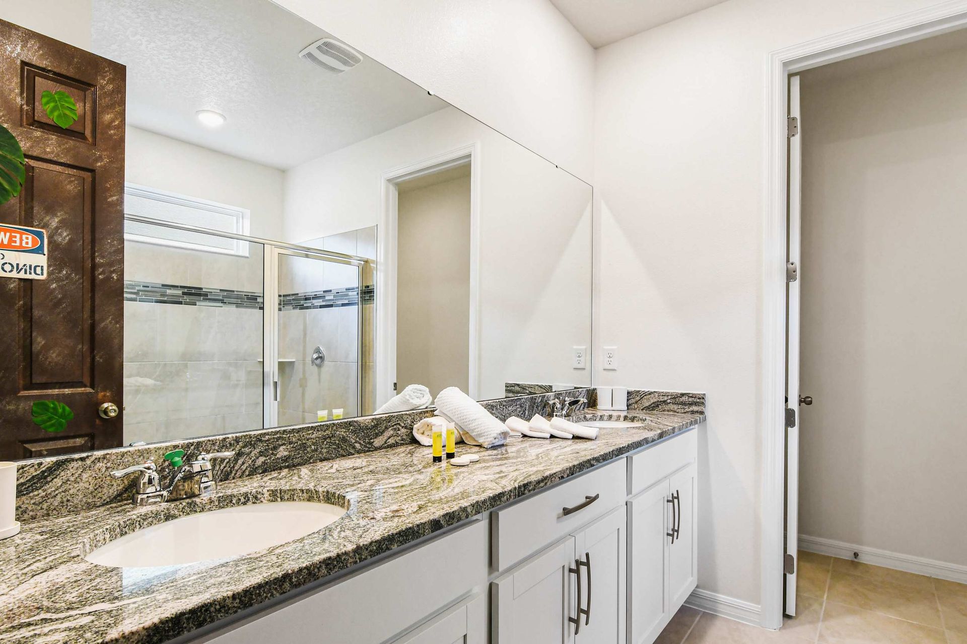 Spacious bathroom with dual sinks, granite counters, large mirror, and glass shower.