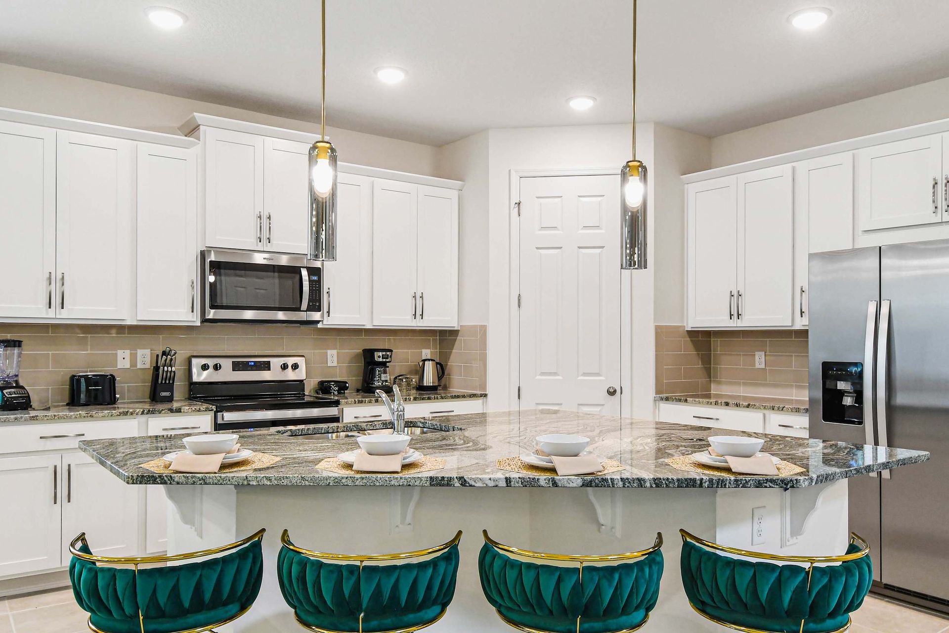 Elegant kitchen with marble island, velvet bar stools, and modern stainless steel appliances.