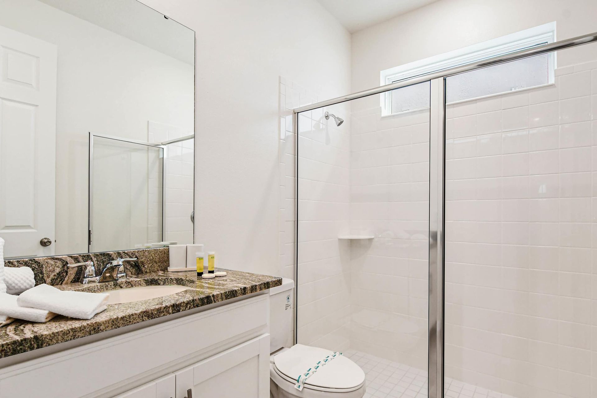 Bright modern bathroom with granite vanity, large mirror, and spacious glass shower.