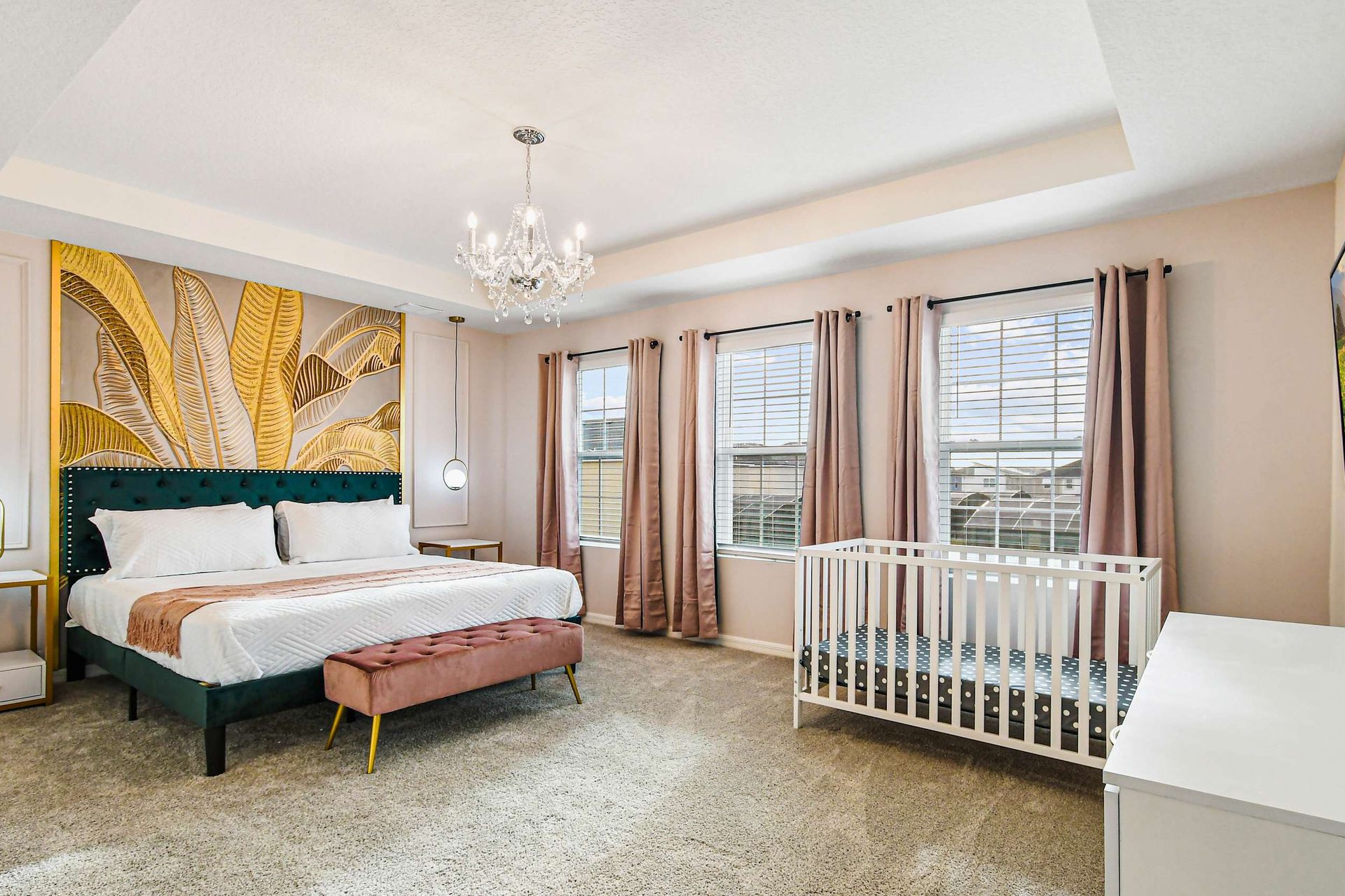 Spacious master bedroom with emerald bed, gold accents, chandelier, and crib setup.