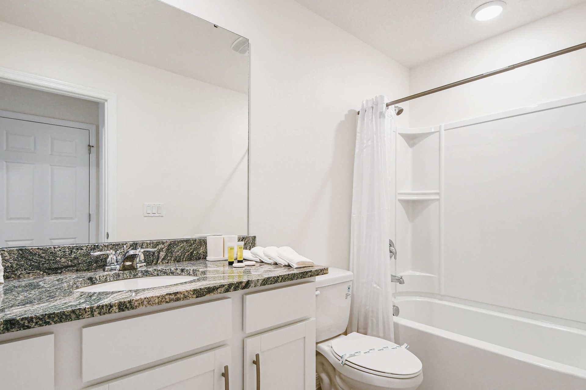 Bright modern bathroom with granite vanity, large mirror, and tub-shower combination.