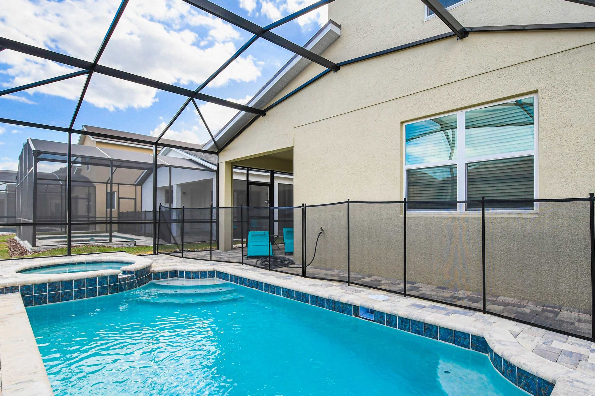 Inviting screened-in pool and spa with safety fence and cozy outdoor lounge space.