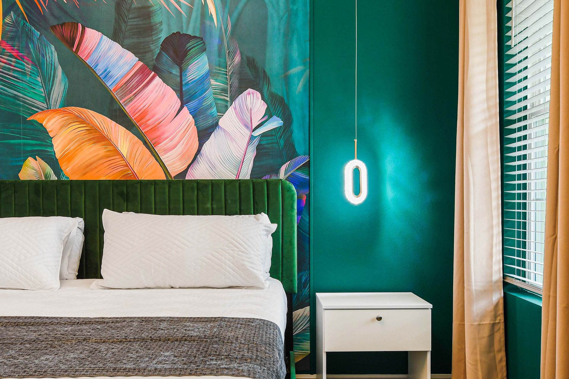 Tropical-inspired bedroom with bold colors, velvet headboard, and modern lighting.