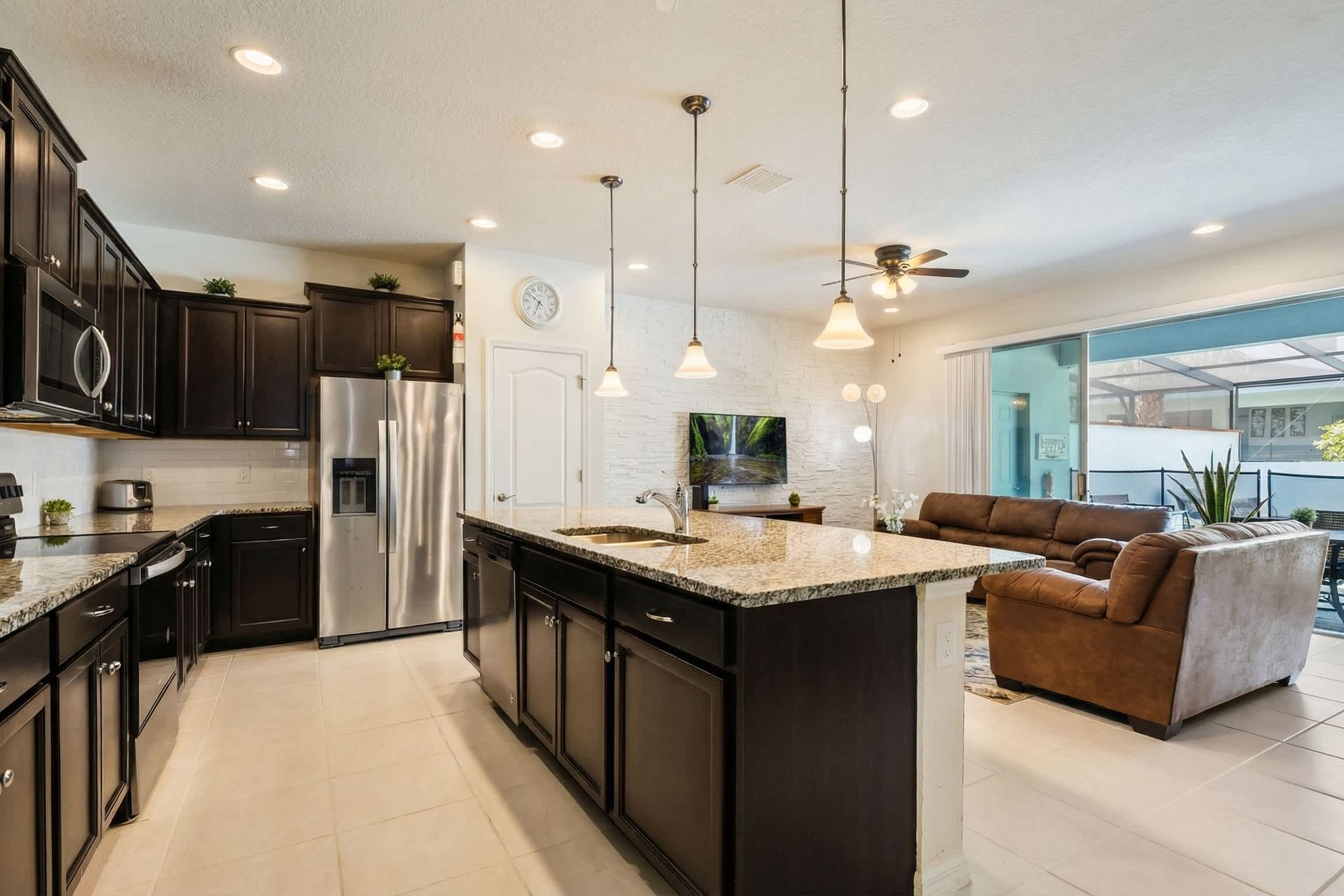 Modern kitchen with granite island, open to a bright living area and poolside views.