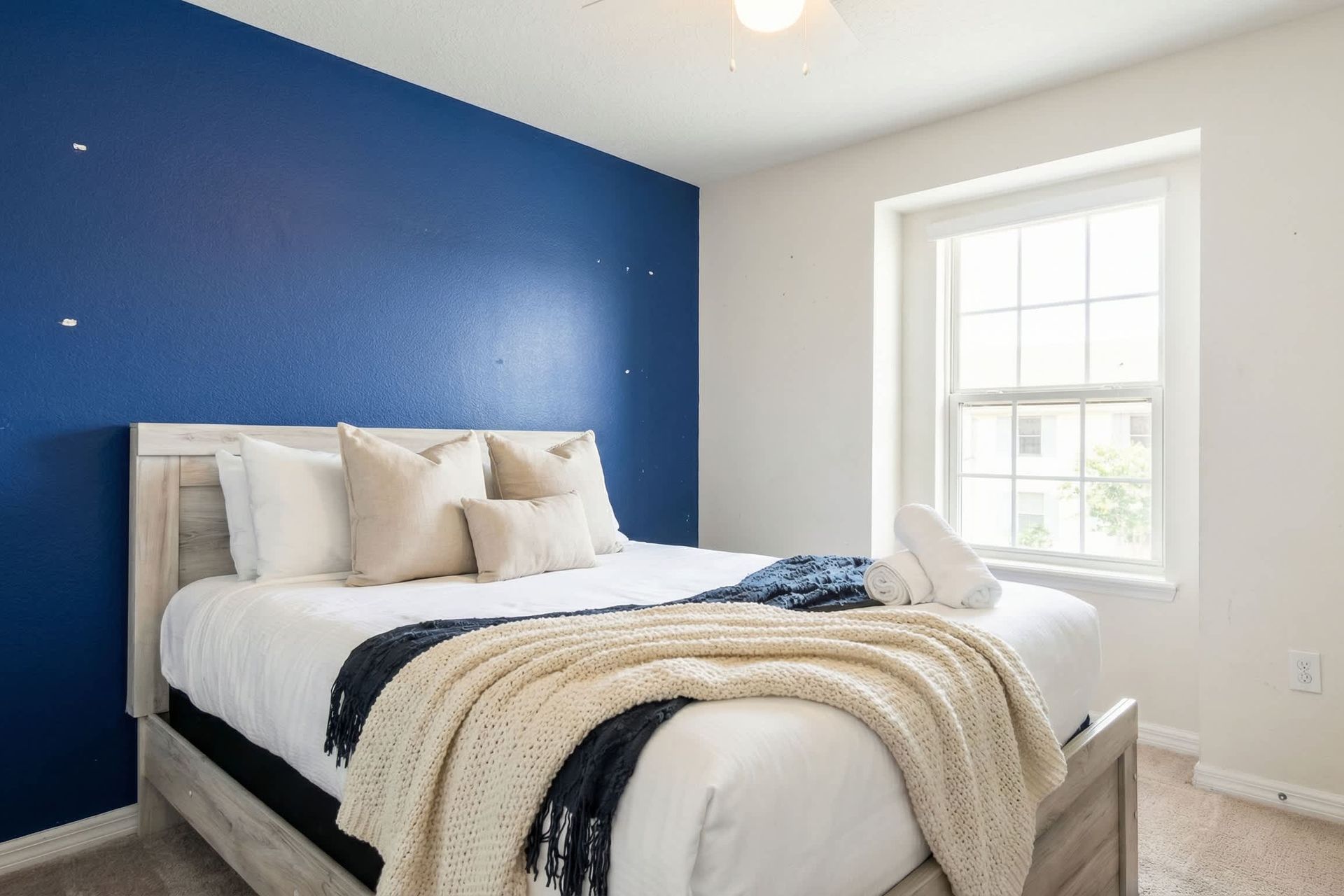 Cozy queen bedroom with bold accent wall and bright natural window light.