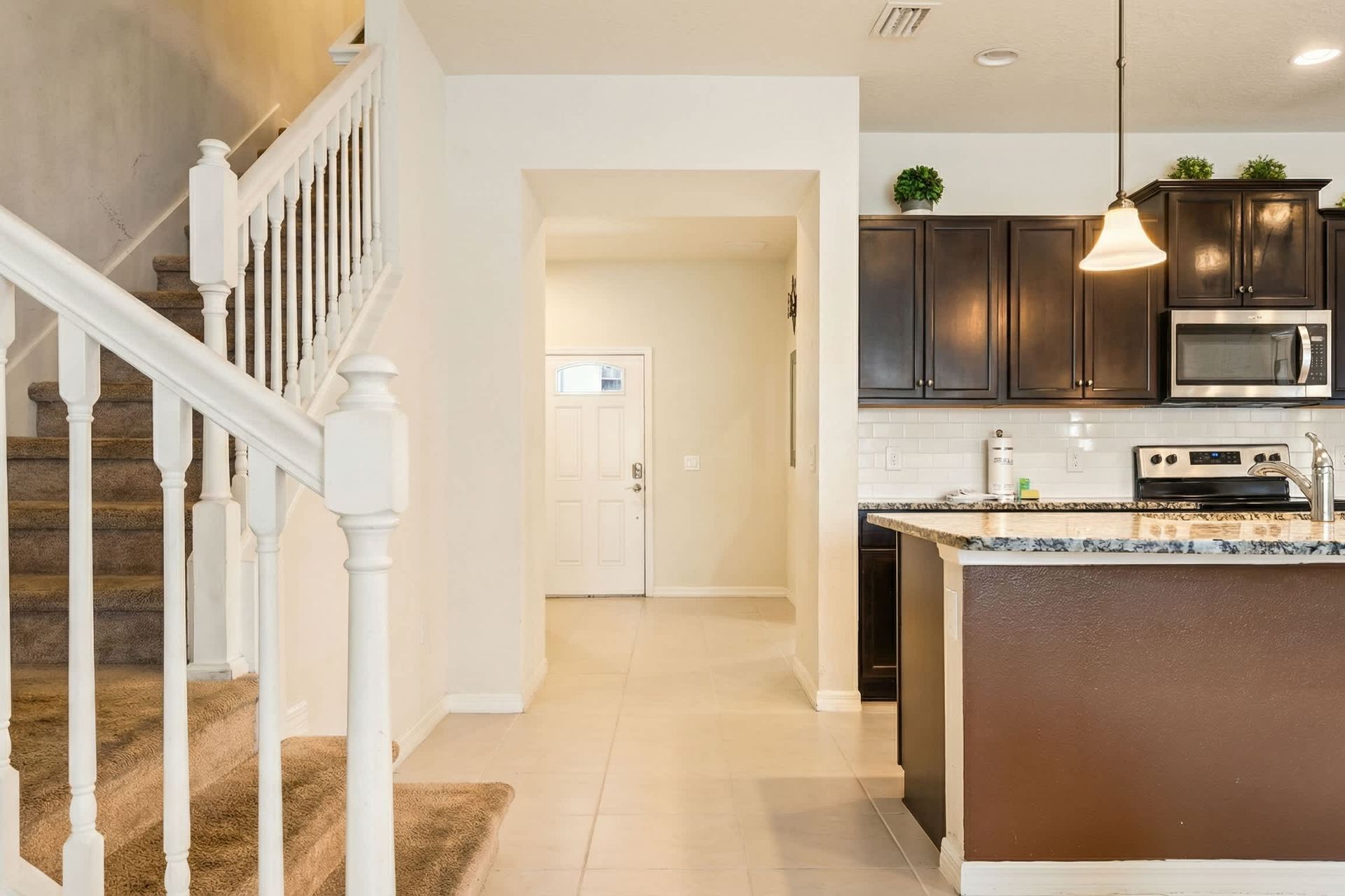 Bright, open entryway leading into a modern kitchen with granite countertops and dark cabinetry.