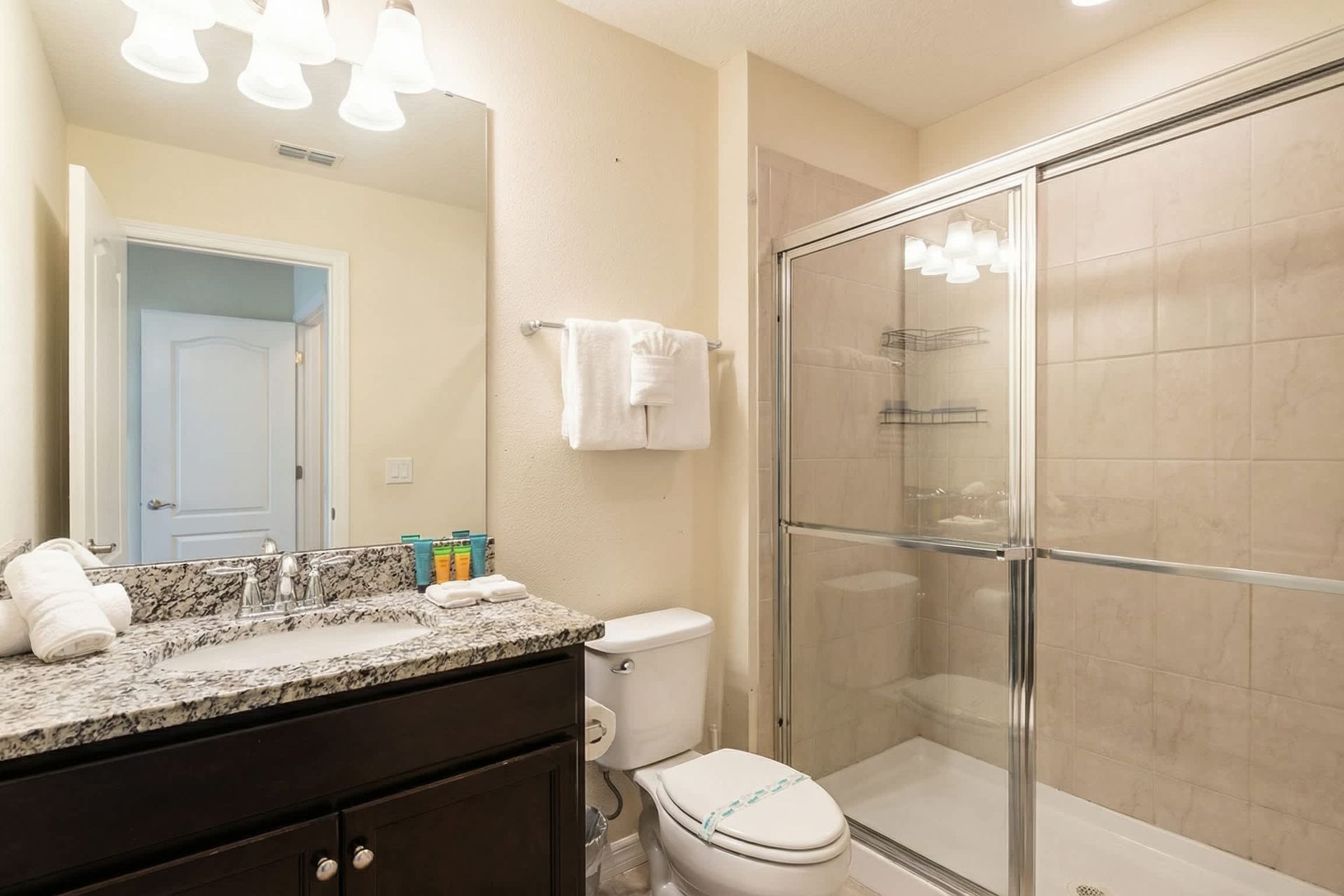 Modern bathroom with granite countertop, dark cabinetry, and a tiled walk-in shower with glass doors.