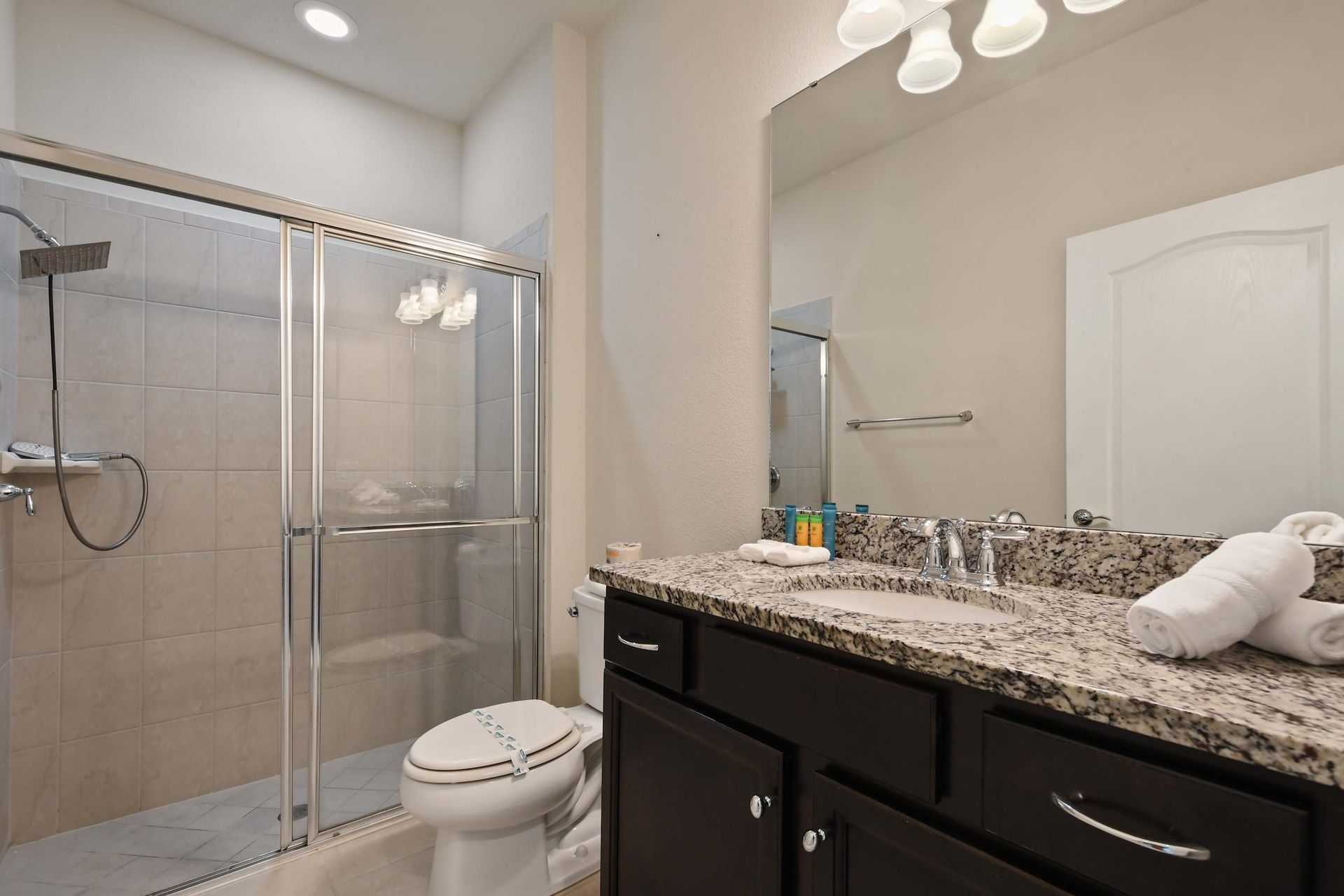 Elegant bathroom featuring a granite countertop, dark wood vanity, and a spacious tiled shower with glass doors. 