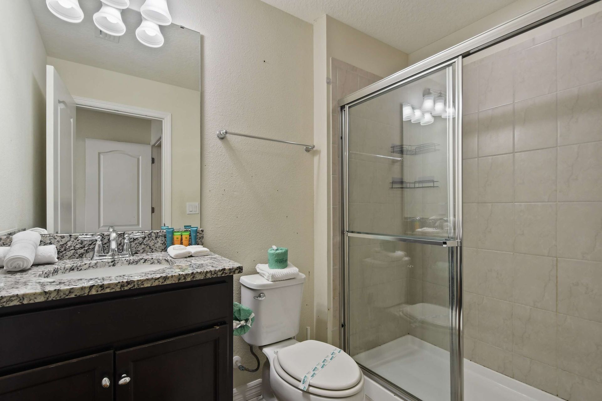 Modern bathroom with granite countertop, dark cabinetry, and a tiled walk-in shower with glass doors.