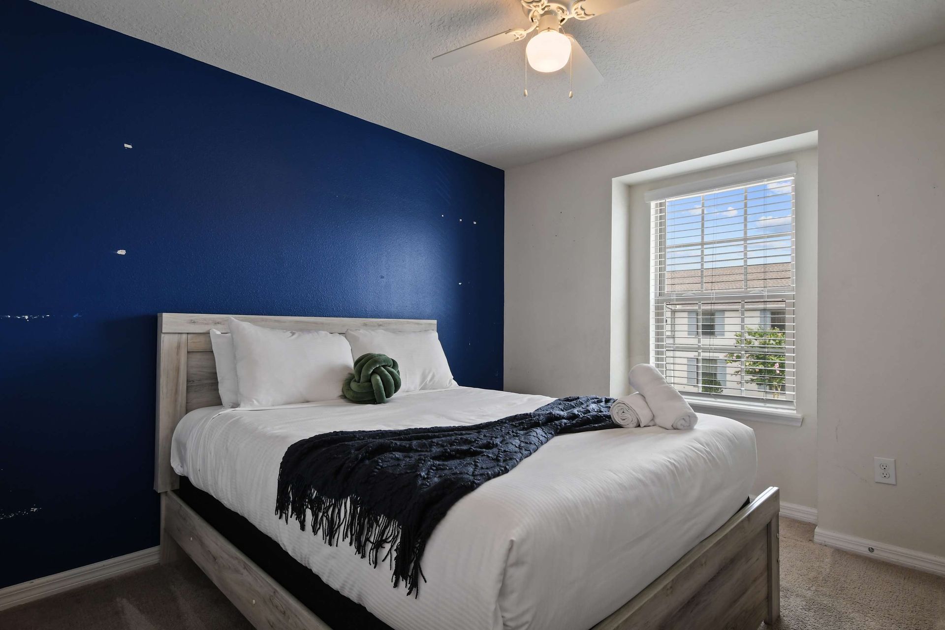 Cozy queen bedroom with bold accent wall and bright natural window light.