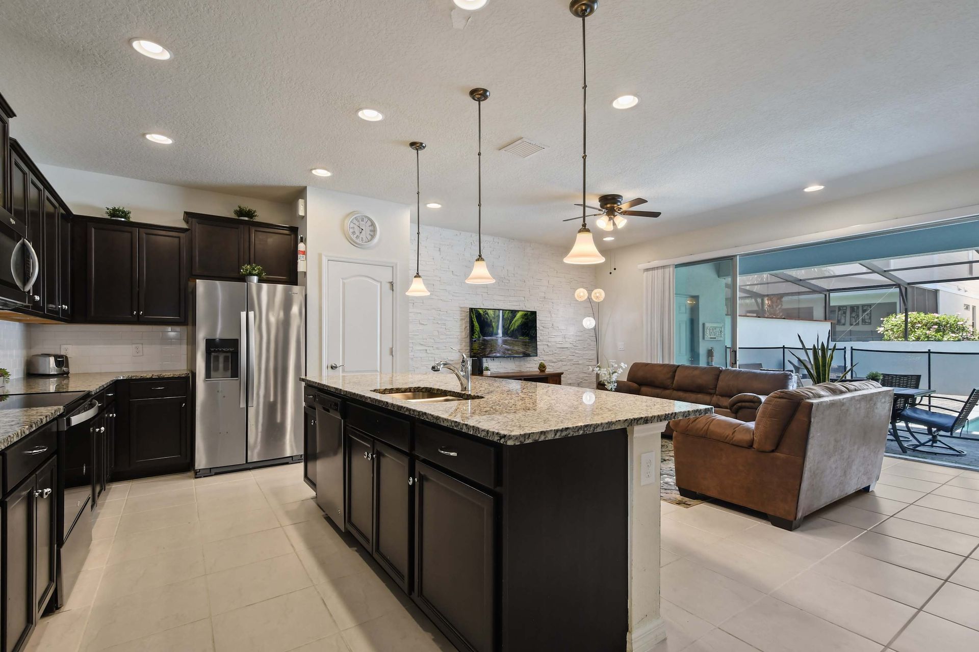 Modern kitchen with granite island, open to a bright living area and poolside views.