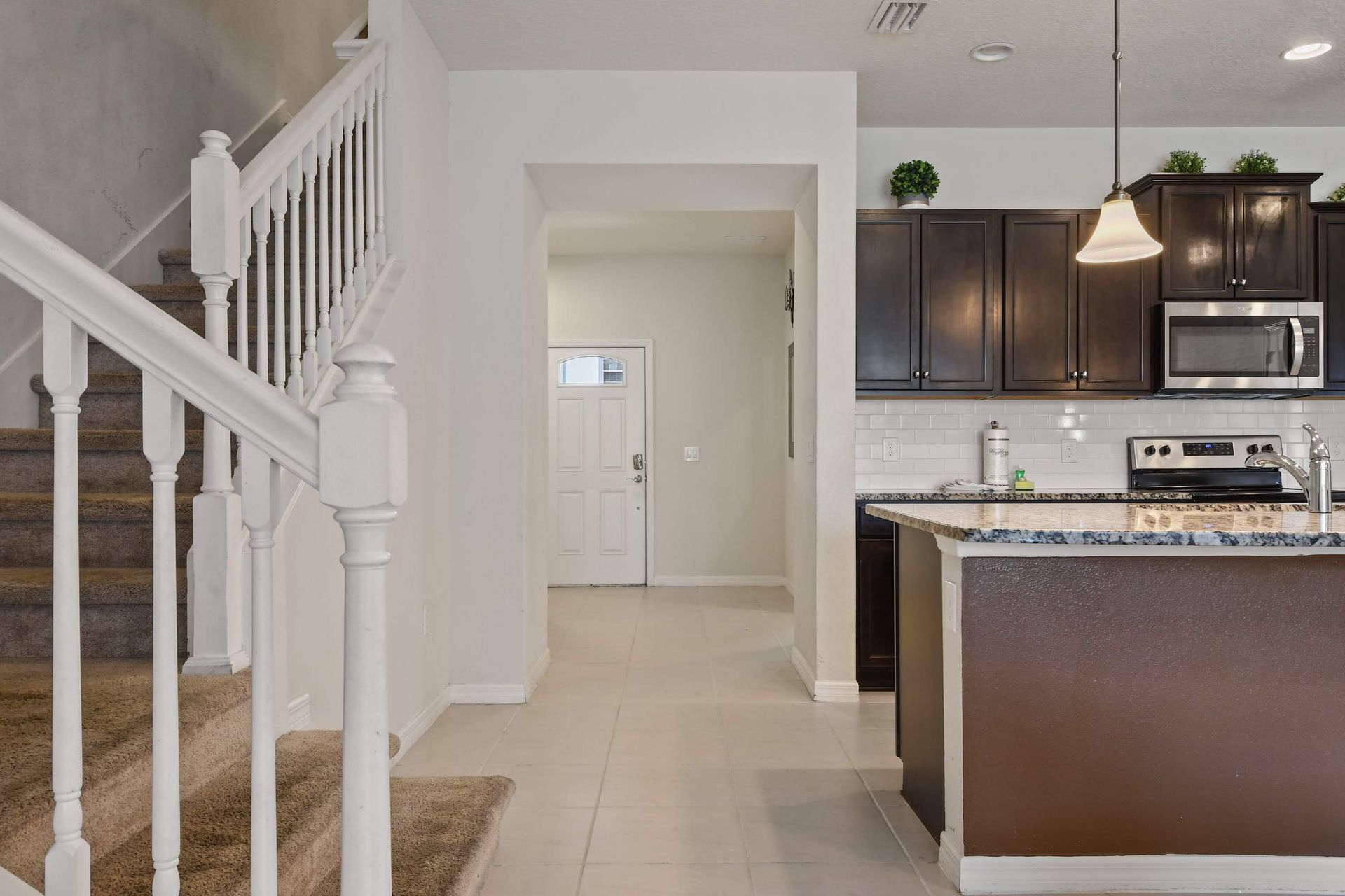 Bright, open entryway leading into a modern kitchen with granite countertops and dark cabinetry.