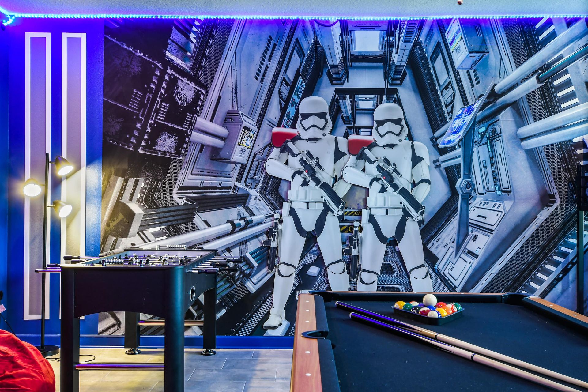 Futuristic game room with themed wall art, foosball, pool table, and LED lights.
