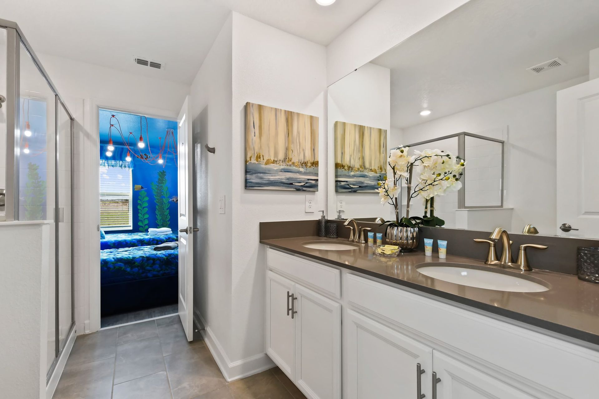 Bright double vanity bathroom with gold finishes and view into themed bedroom.