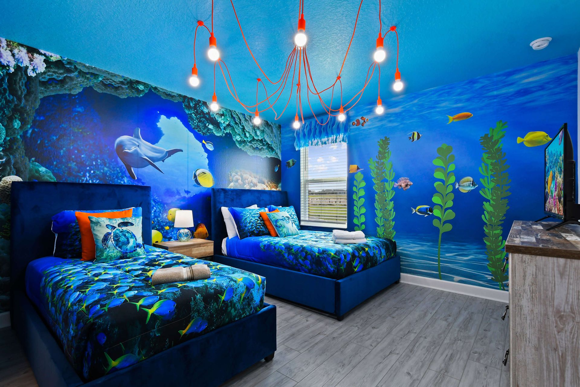 Underwater-themed twin room with ocean murals, vibrant bedding, and playful lighting.