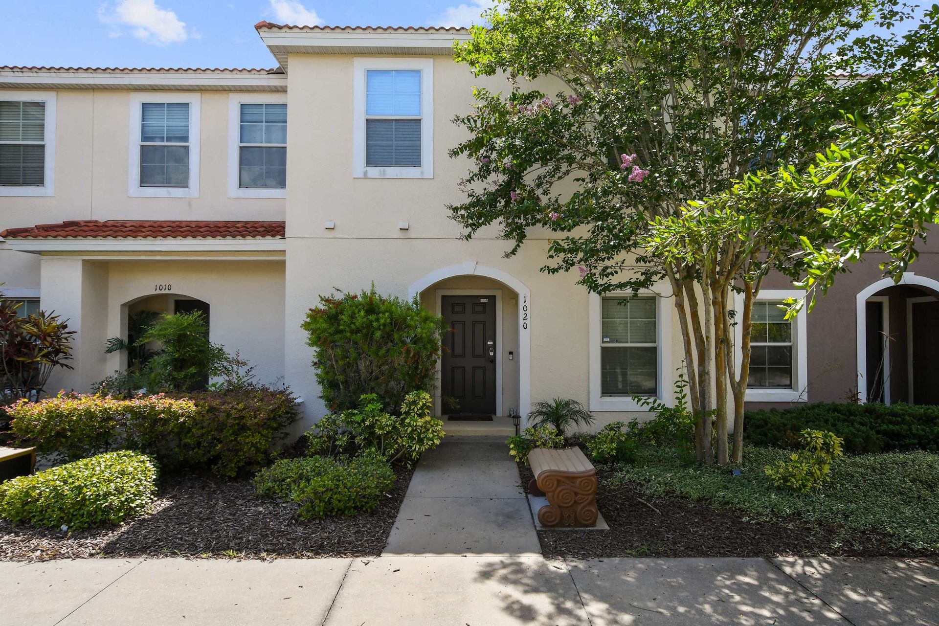 Charming townhouse with lush landscaping and a cozy front bench!