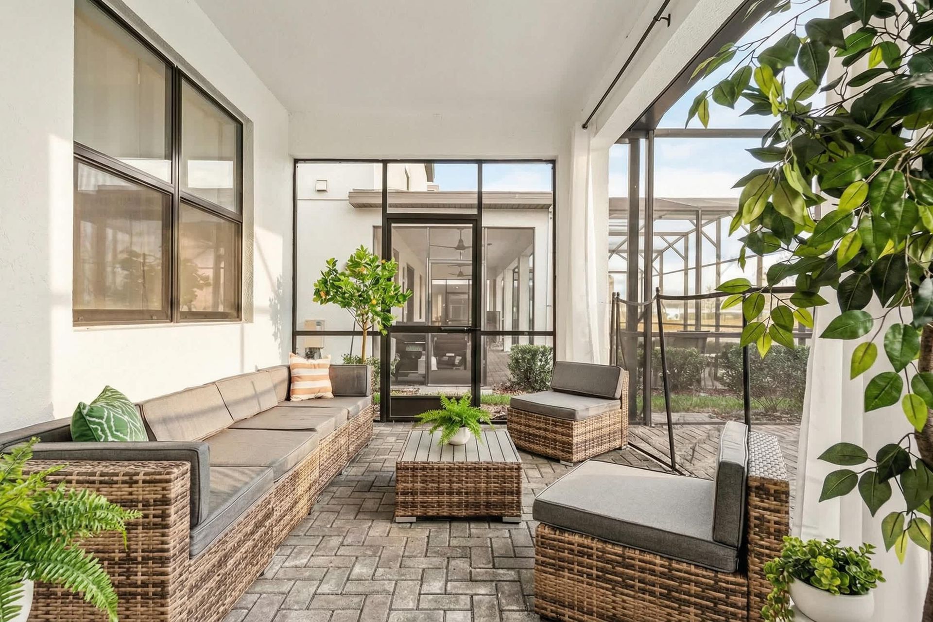 Cozy screened-in patio with stylish wicker seating, lush greenery, and a relaxing vibe.