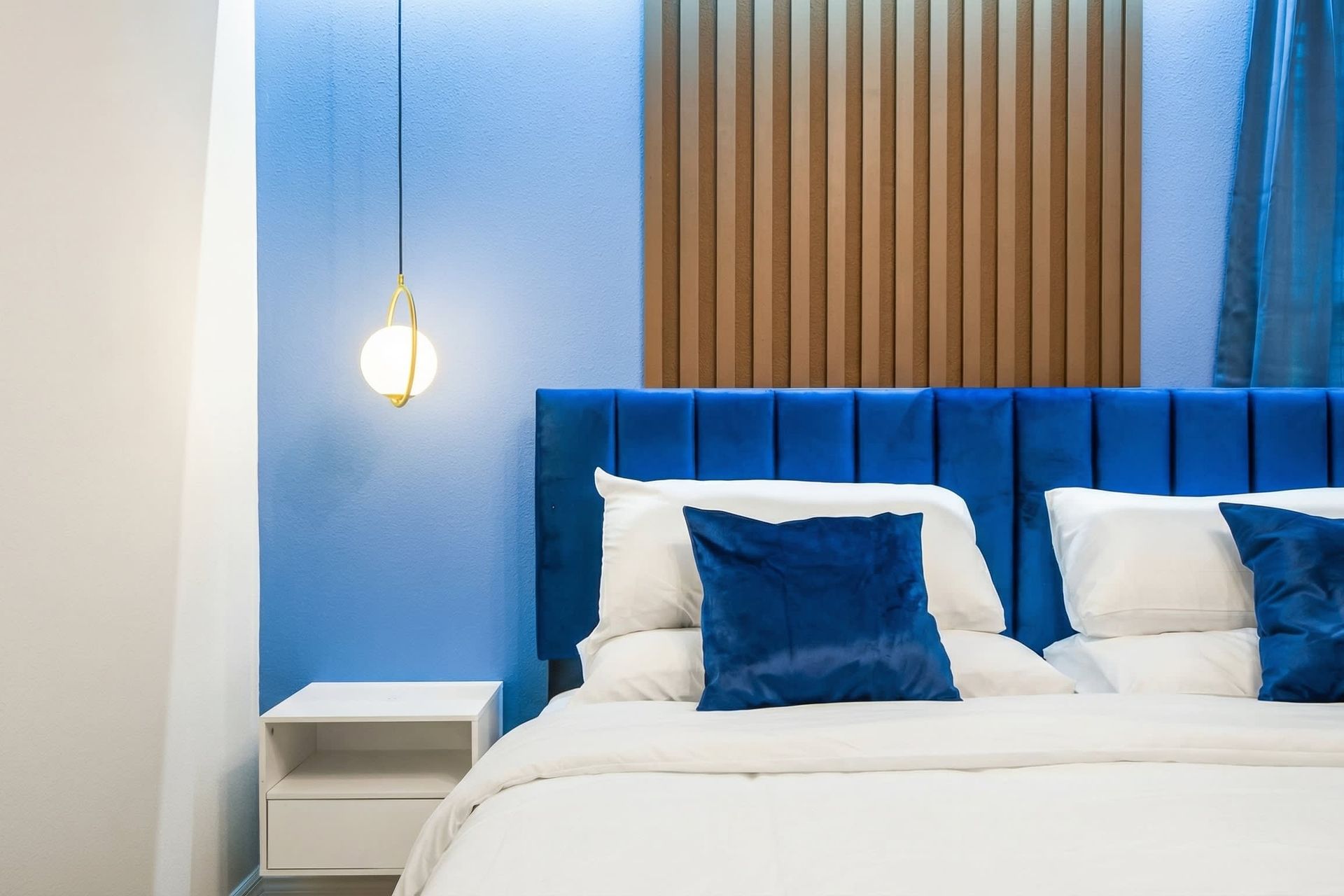 Luxurious blue velvet headboard, glowing accent wall, and elegant hanging light.